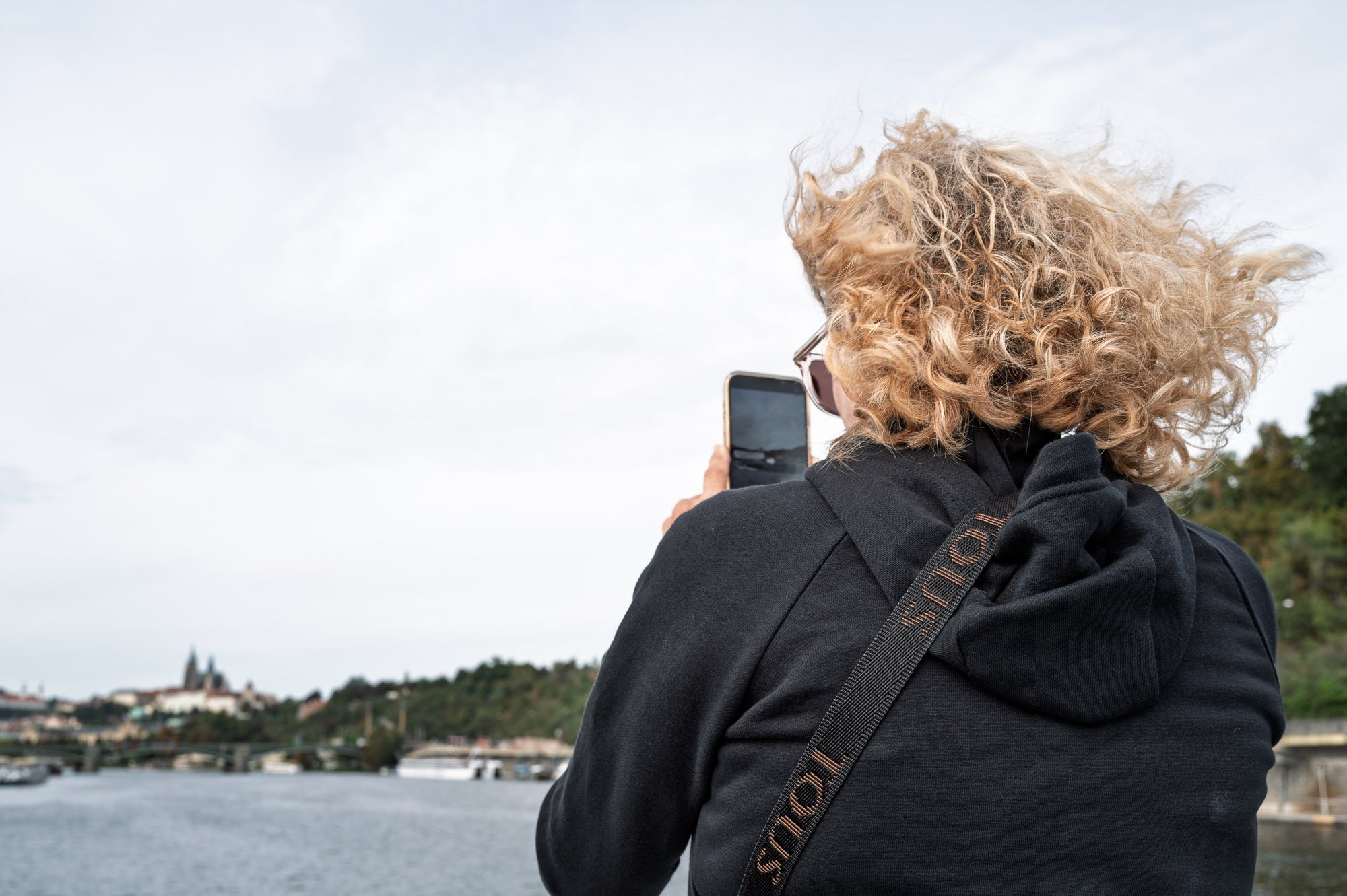 Woman with windblown curls filming Prague Castle across the Vltava — Leica Q3