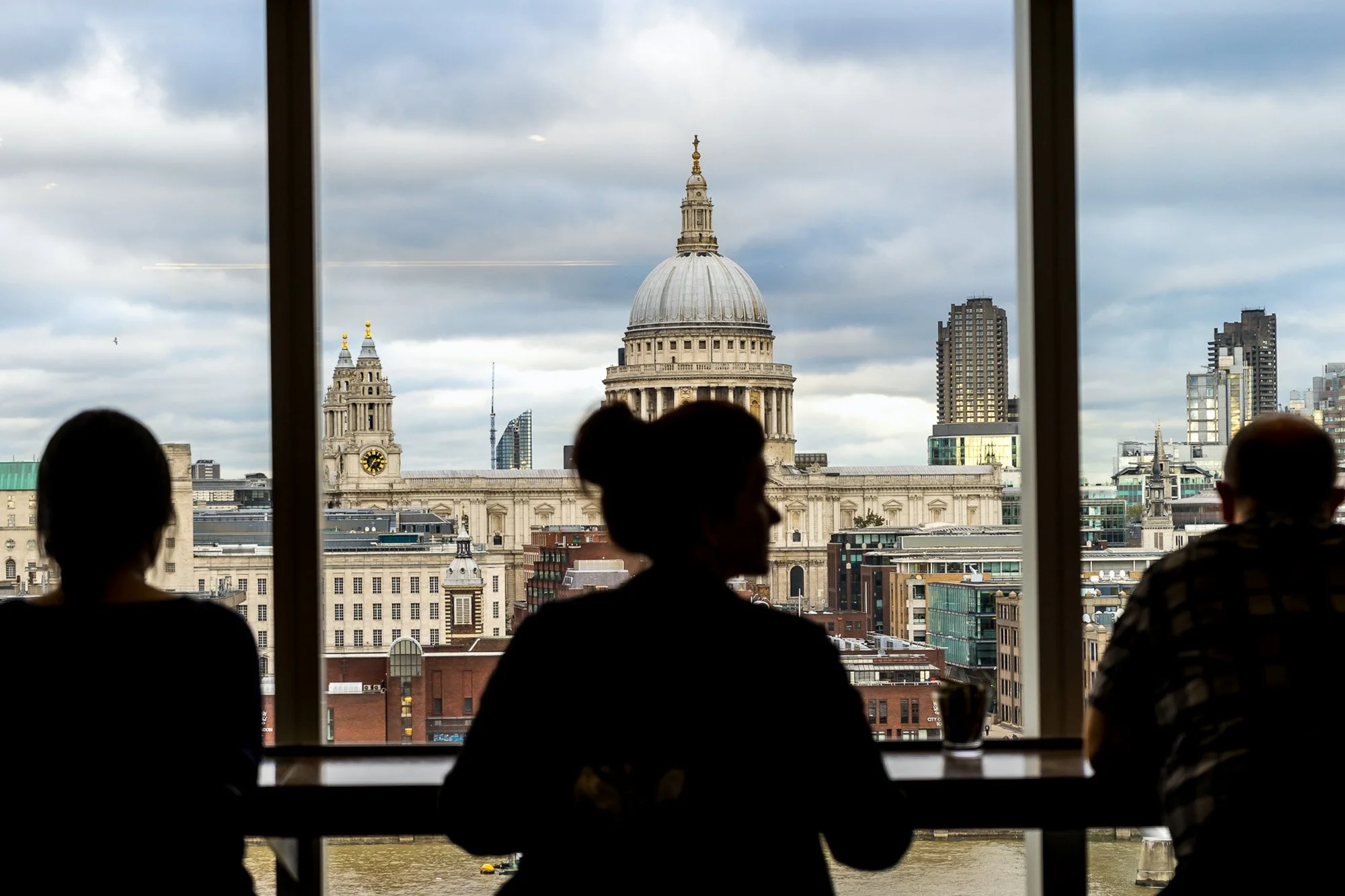 Three silhouetted figures seated by a window overlooking St. Paul's Cathedral and the London skyline from the Tate Modern — bCLPhoto