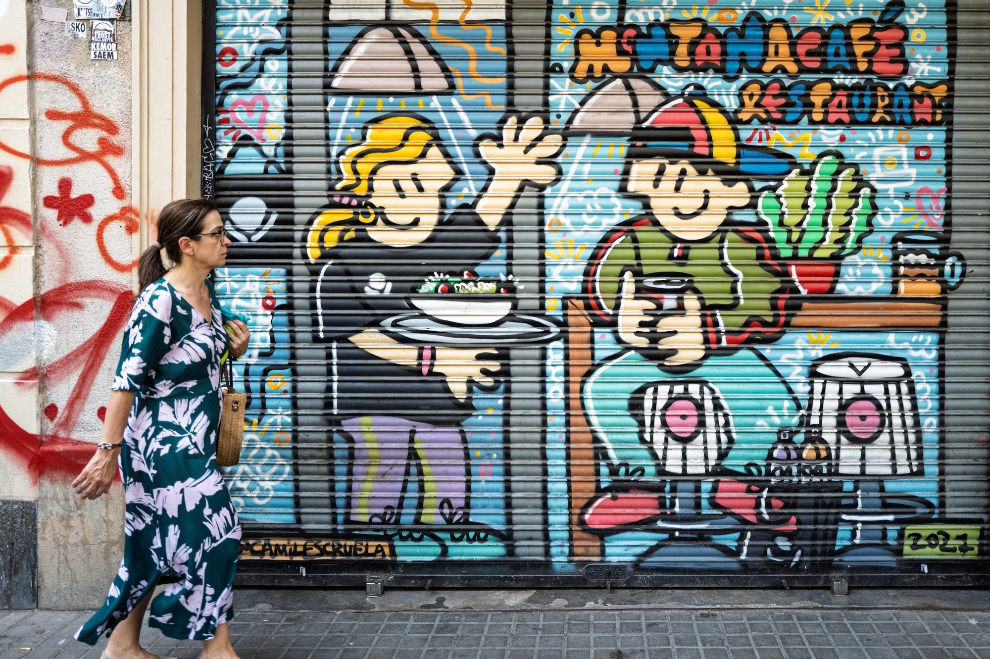 Colourful comic-style mural on a restaurant shutter in El Born, Barcelona, with a woman walking past