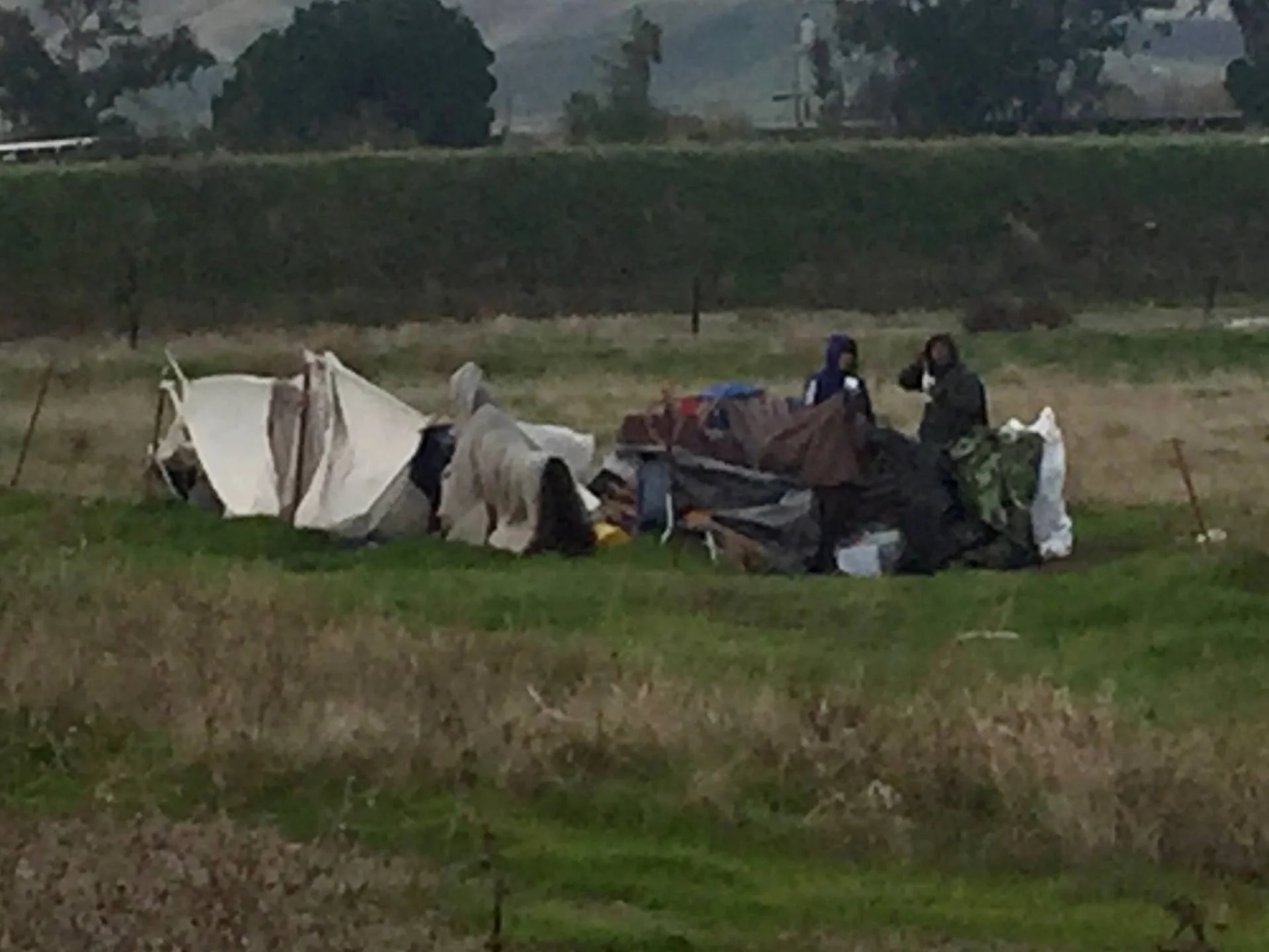 Scene of a crash site with a toppled vehicle and emergency responders investigating in a grassy area during daytime.