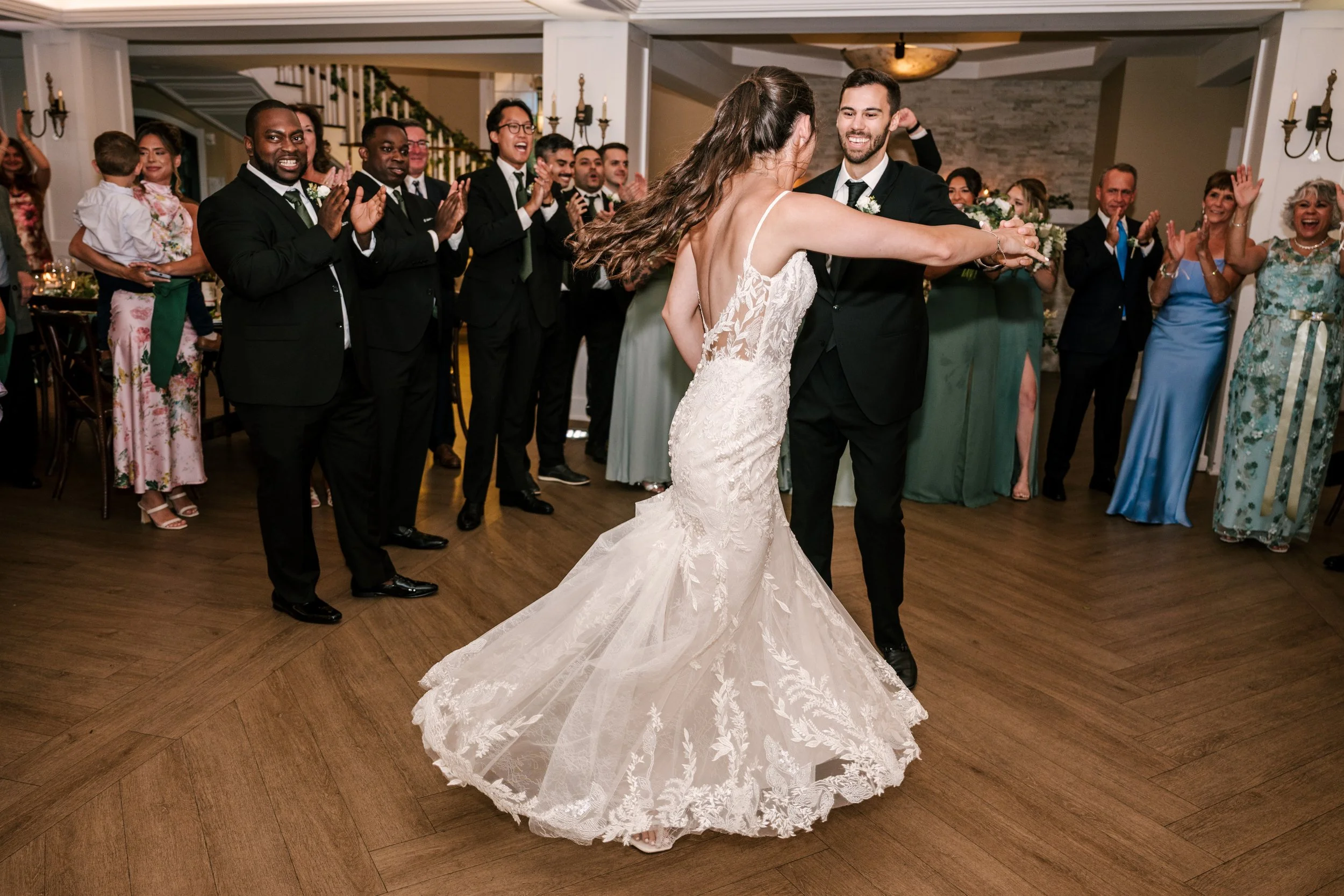 A bride and groom are dancing at a wedding reception while surrounded by happy guests clapping and celebrating.