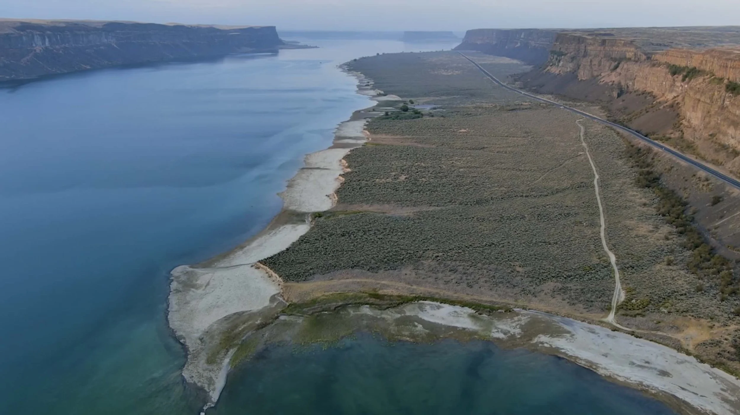Aerial view of a large river flowing between steep cliffs with areas of shoreline and sparse vegetation.