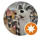 Costumed character waving inside a store, wearing a plaid shirt. Orange star icon on the image.