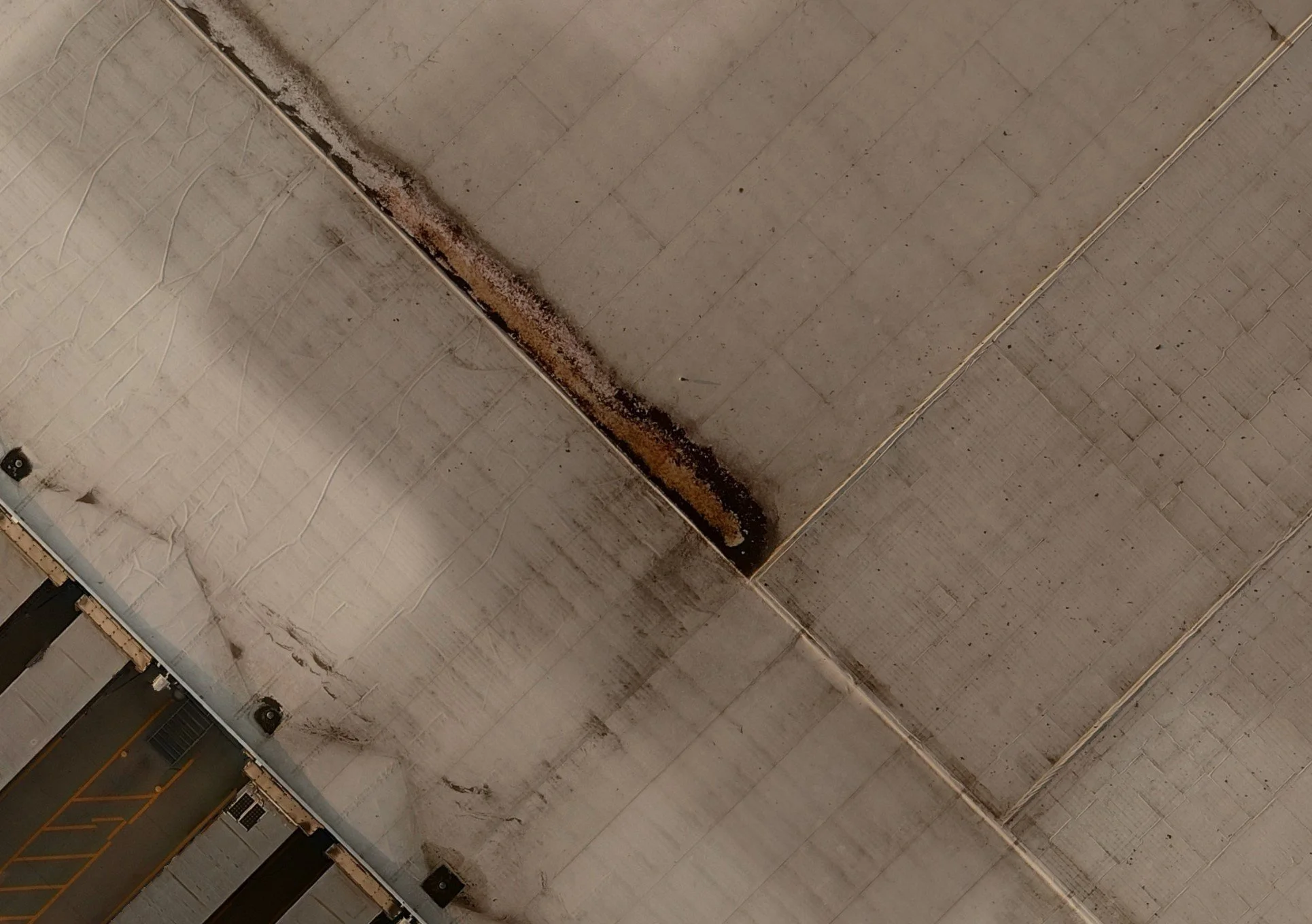 Aerial view of a large building roof with visible dirt and wear along the seams.