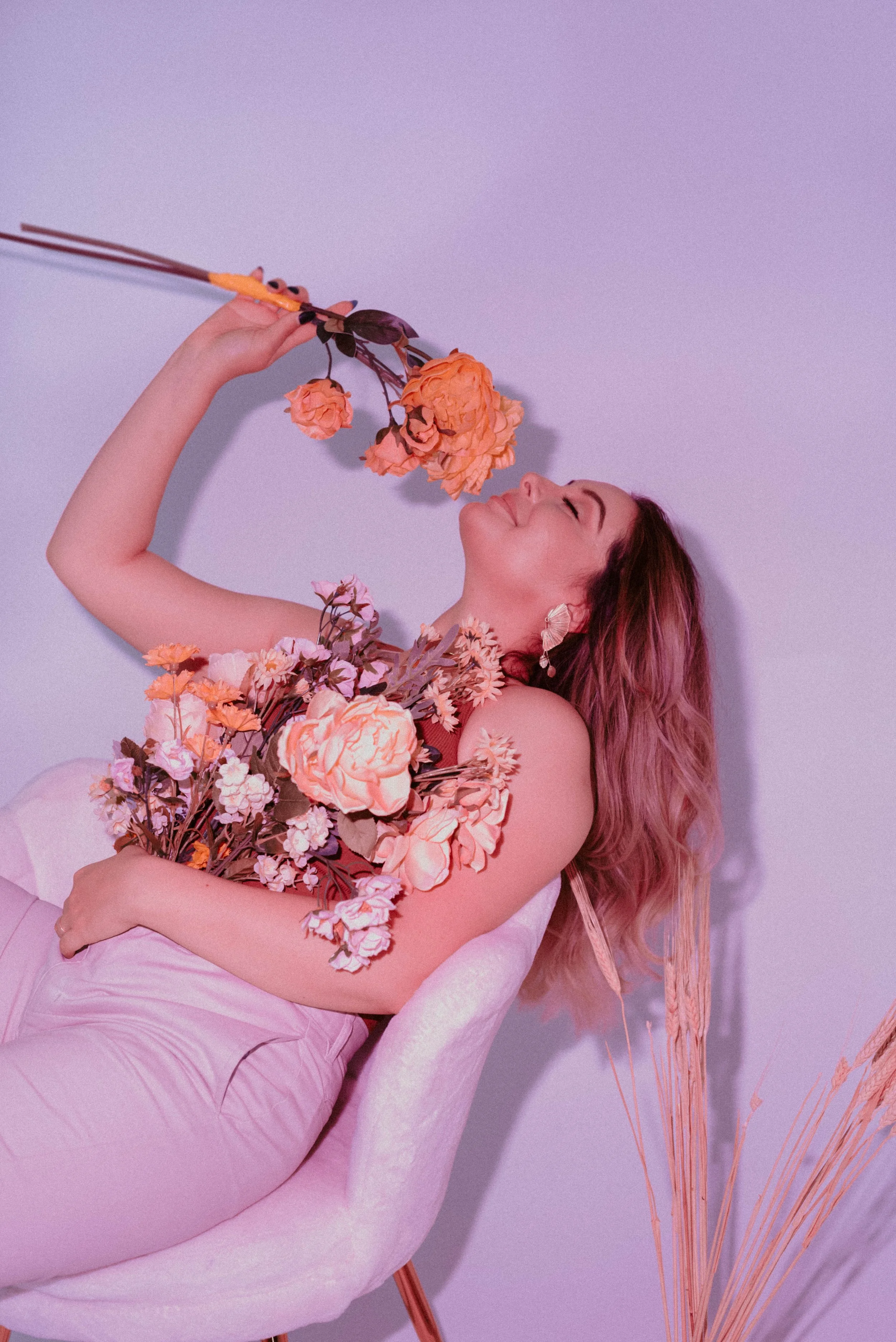 Jojo leaning back in chair with flower bouquet in her arms and smelling one of the flowers in her right hand.