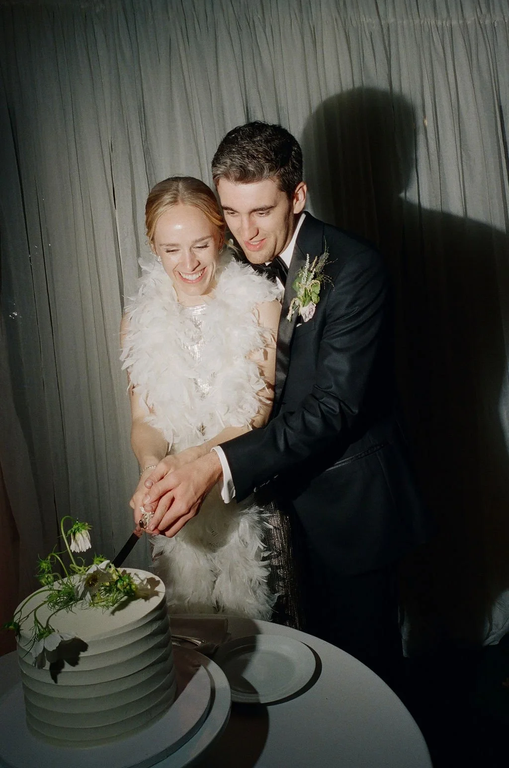 A bride and groom smiling and cutting a wedding cake together.