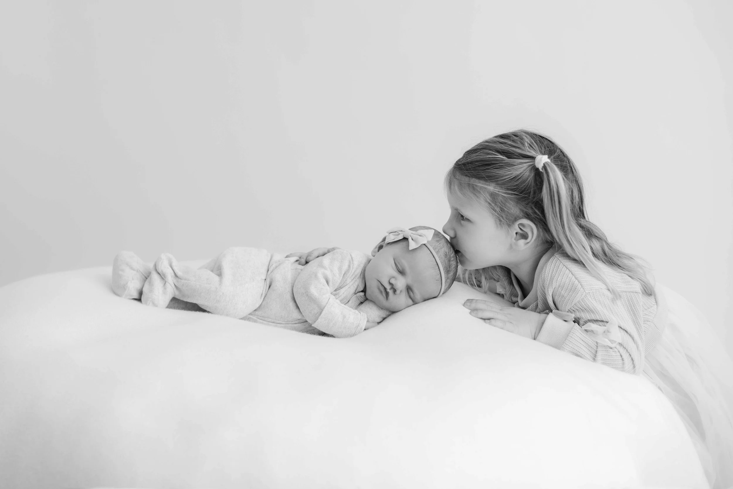 Newborn being kissed on the head by its older sister in Tauranga studio