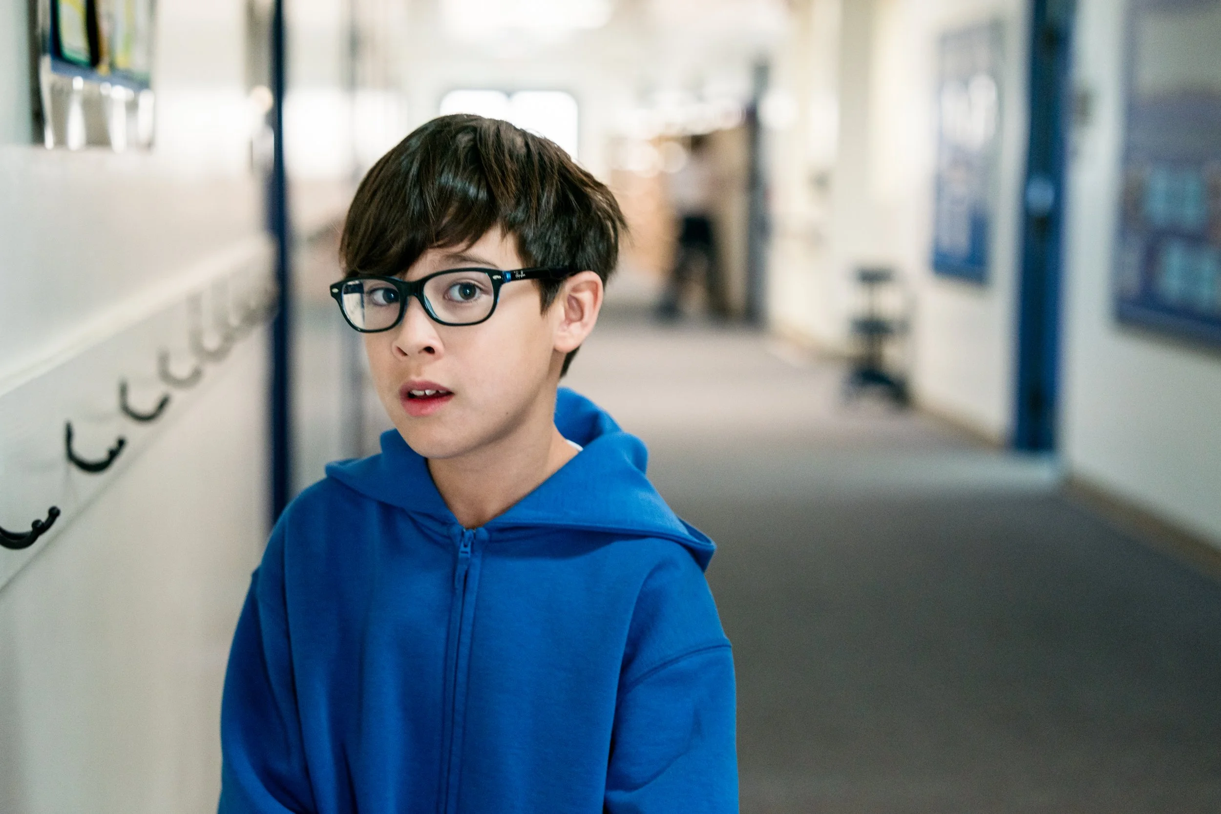 Pathway elementary student with glasses and a blue hoodie in the school hallway