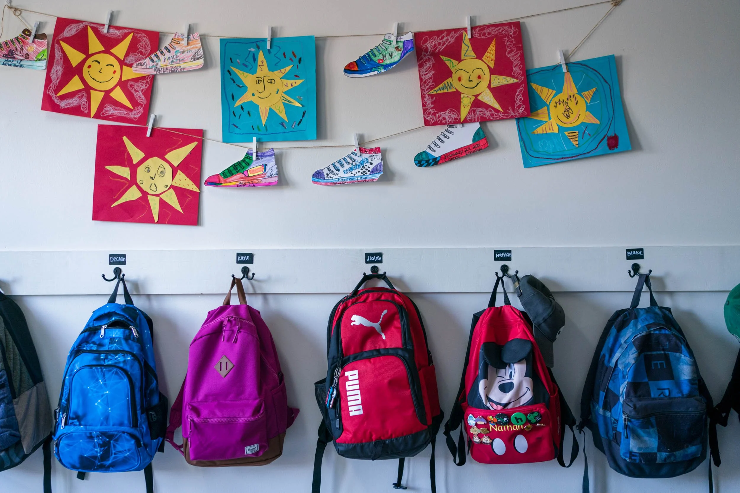 Student backpacks hanging below colorful sun artwork in a Pathway classroom