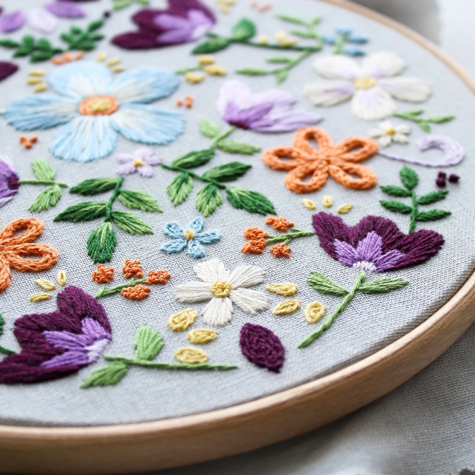 Finished Penelope floral hand embroidery hoop featuring folk style flowers stitched with satin stitch and French knots.