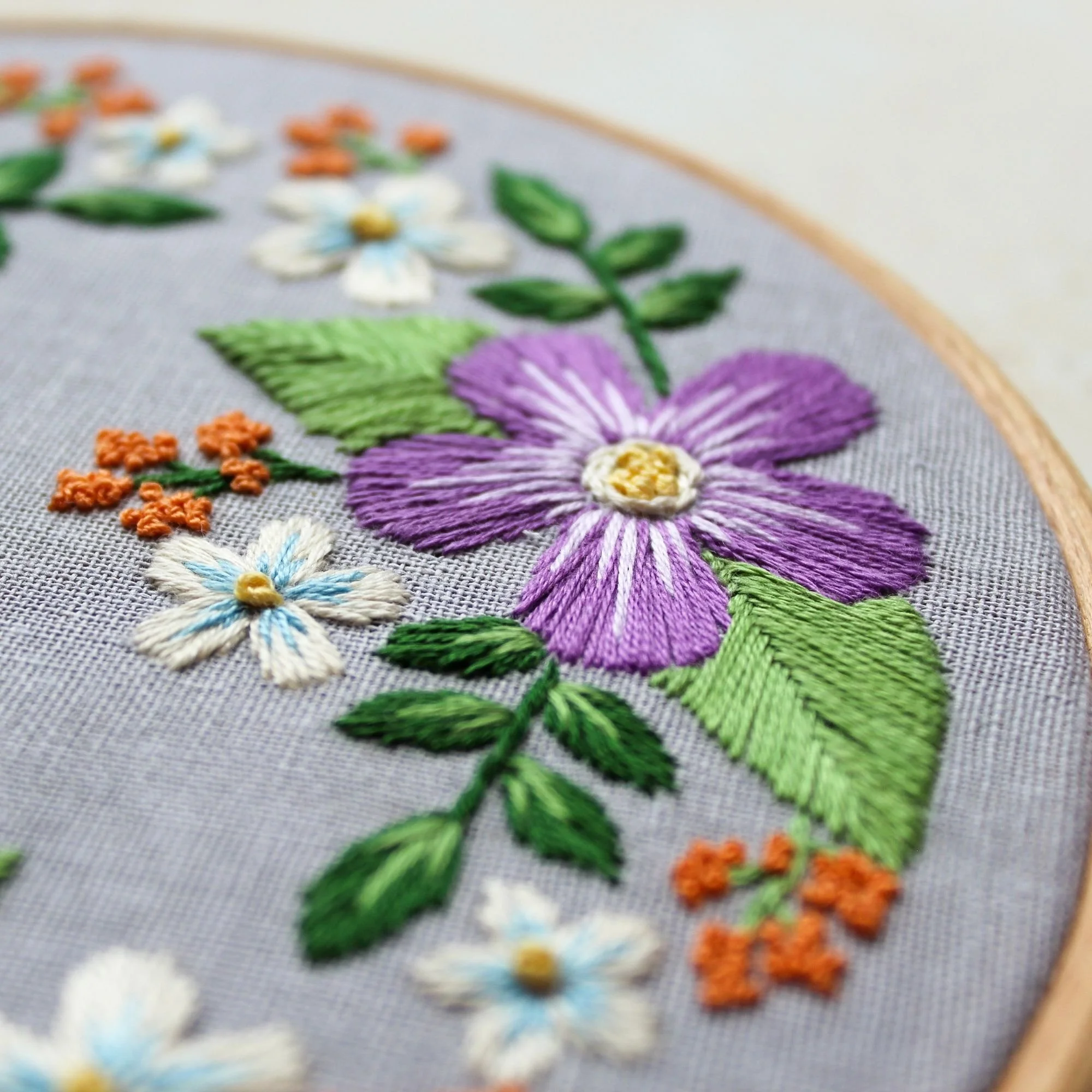 Close-up detail of purple satin stitch flower and green fishbone leaves in the Daphne Folk Garden embroidery pattern.