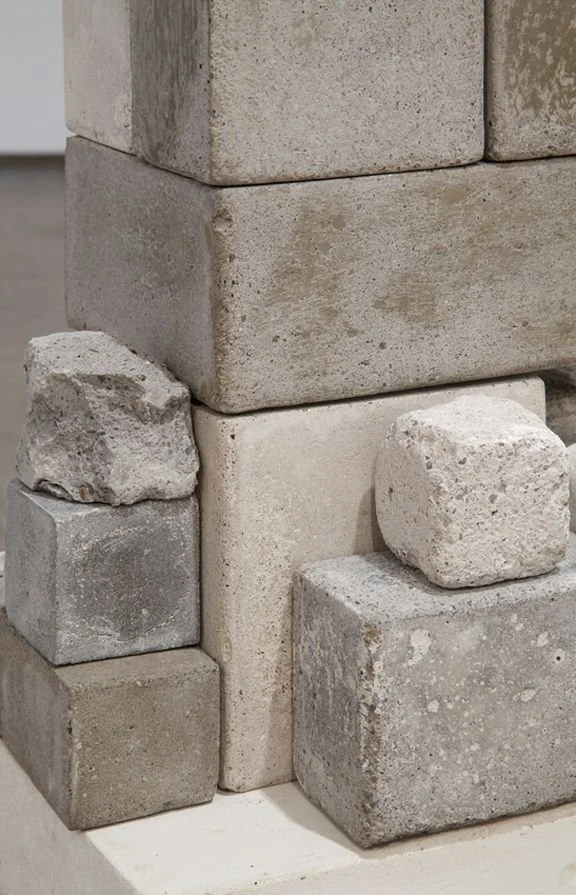 A close-up of various stacked concrete blocks and bricks in different sizes and textures, forming part of a structure.