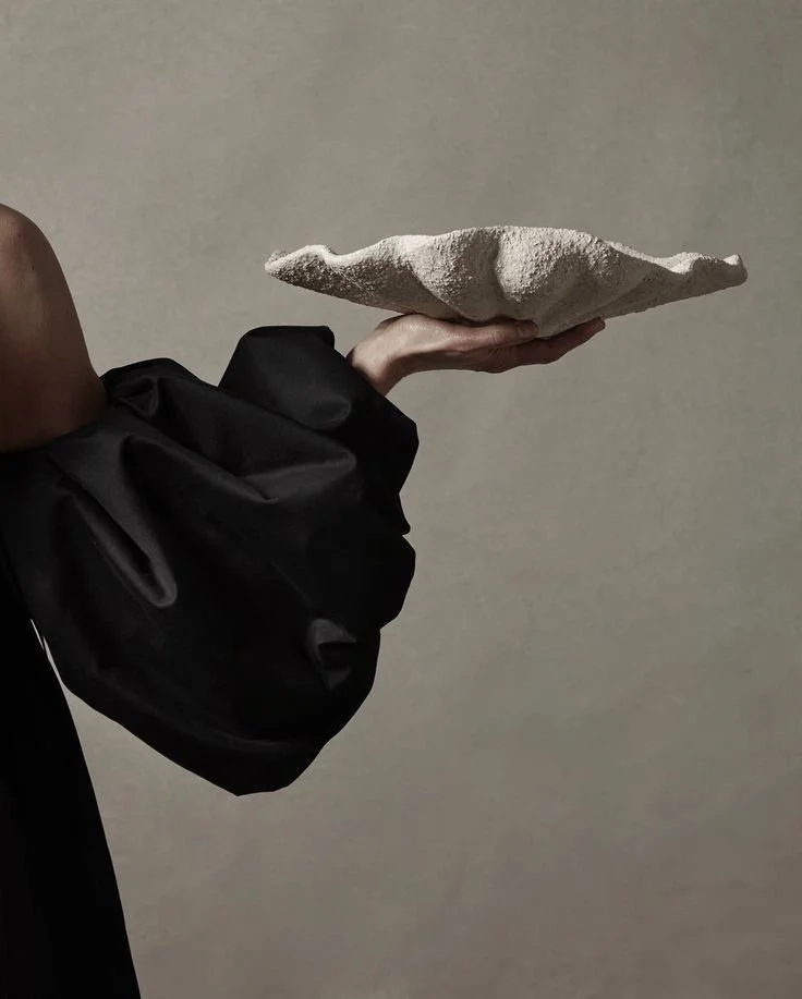 A person holding a large, flat, textured stone plate against a plain, beige background.