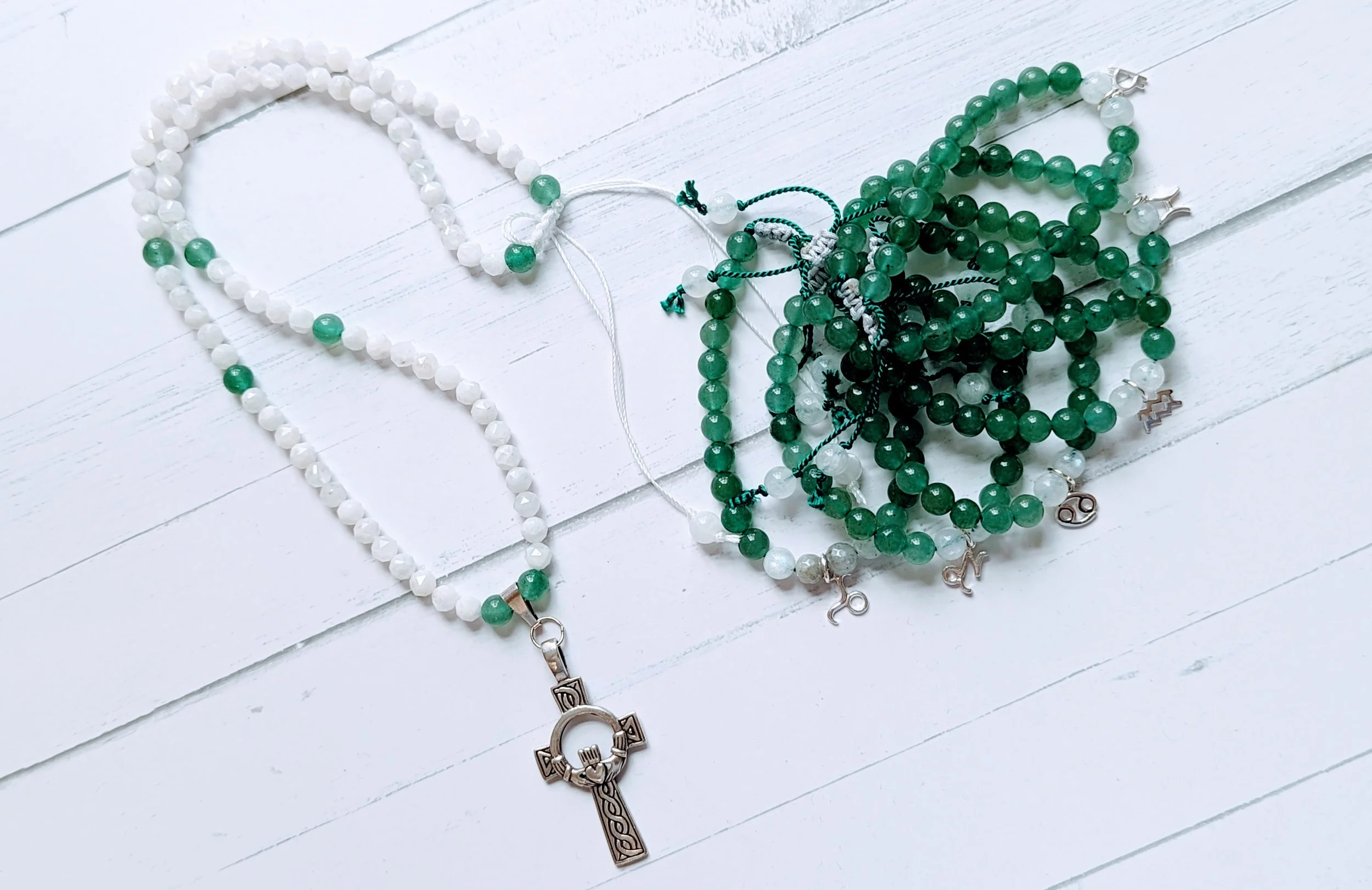 Beaded necklaces with rosary and zodiac signs charms on a white wooden surface.