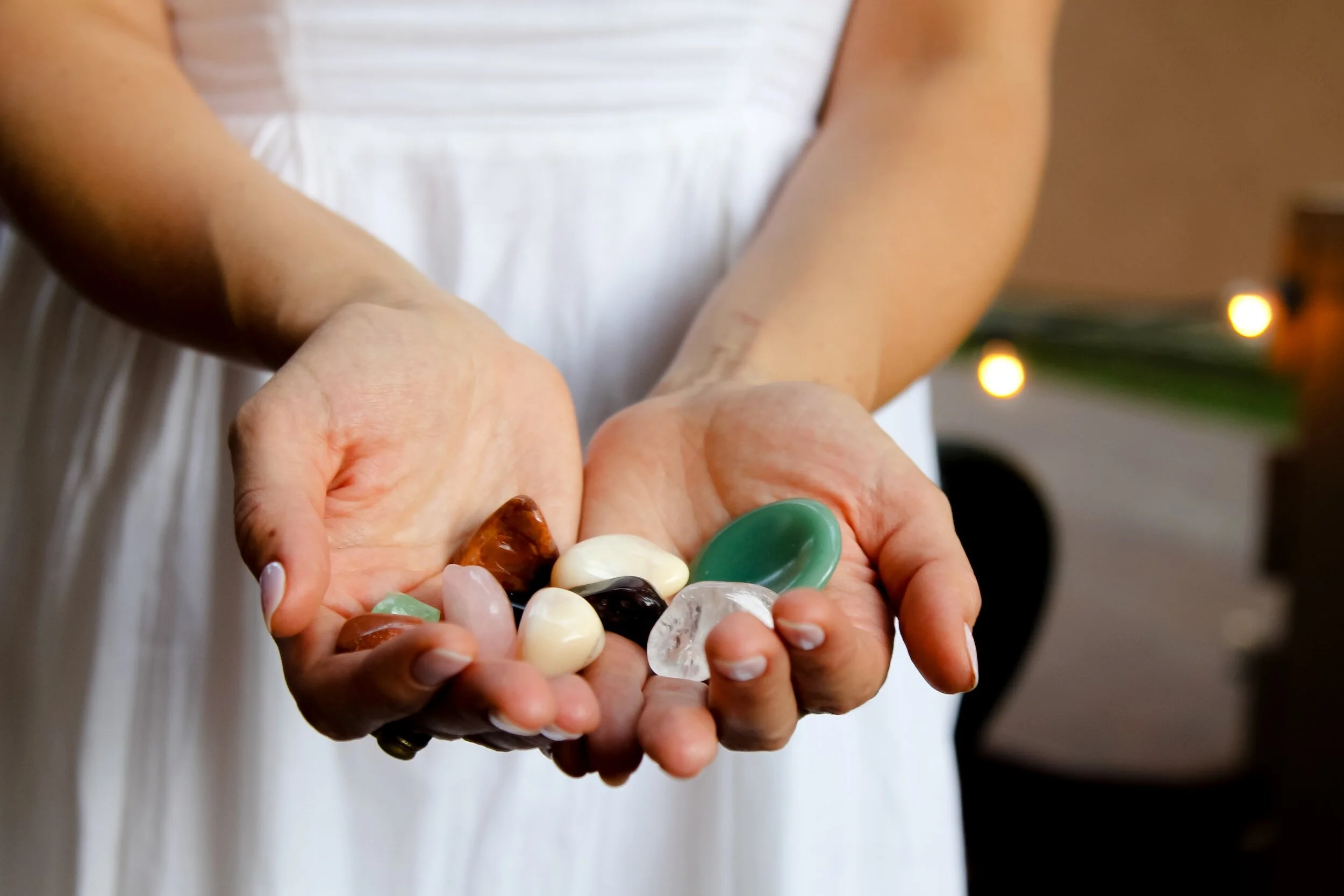 Person holding a variety of colorful glass gemstones or decorative stones in palms.