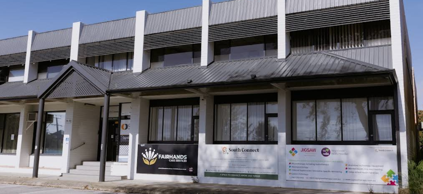 Exterior of a multi-story building with signage for FairHands Care Services, South Connect, and JIGSAW NDIS, featuring large windows and stairs leading to the entrances.