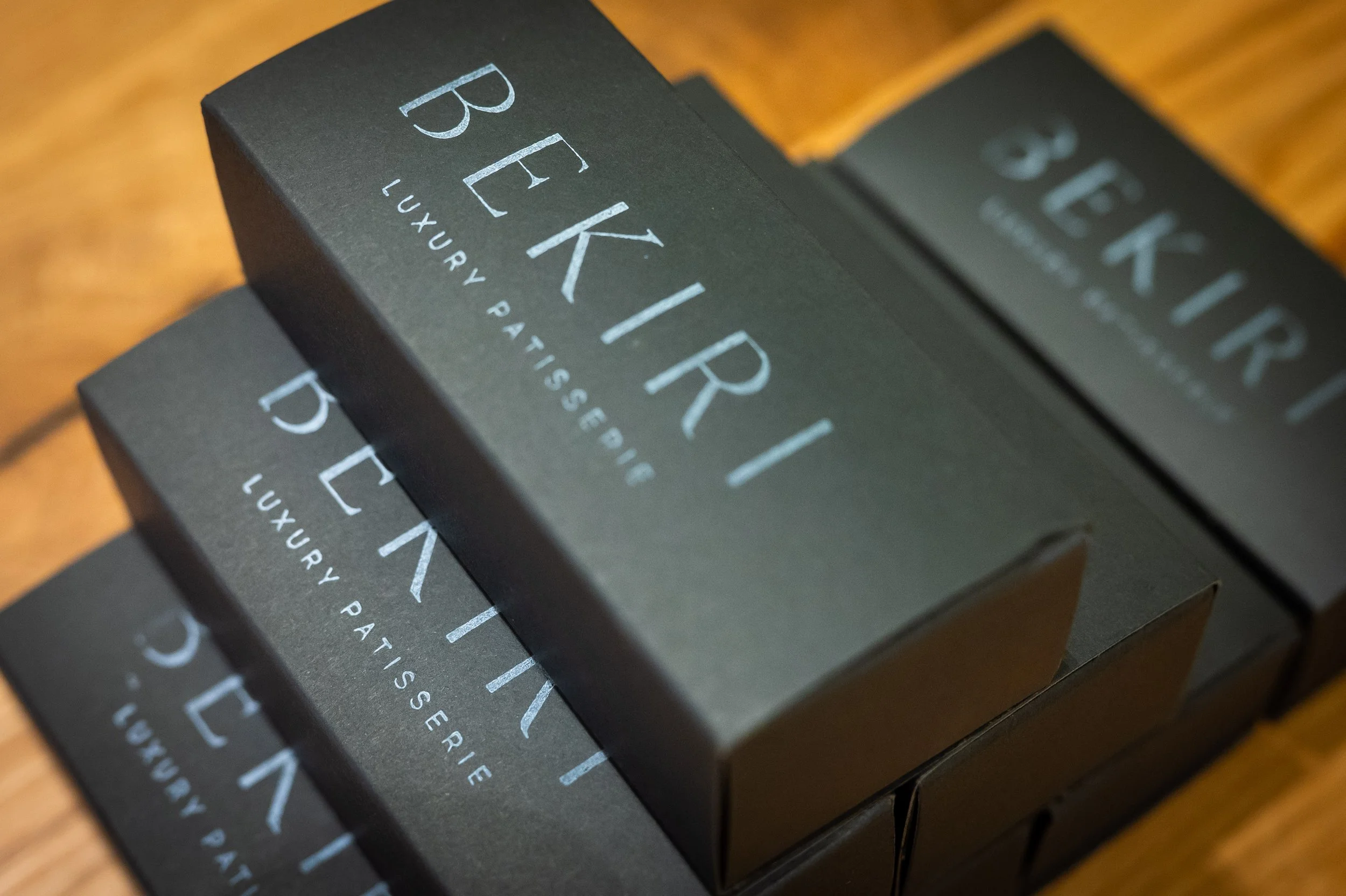 Three black boxes of BEKIRI luxury pâtisserie stacked on a wooden surface.