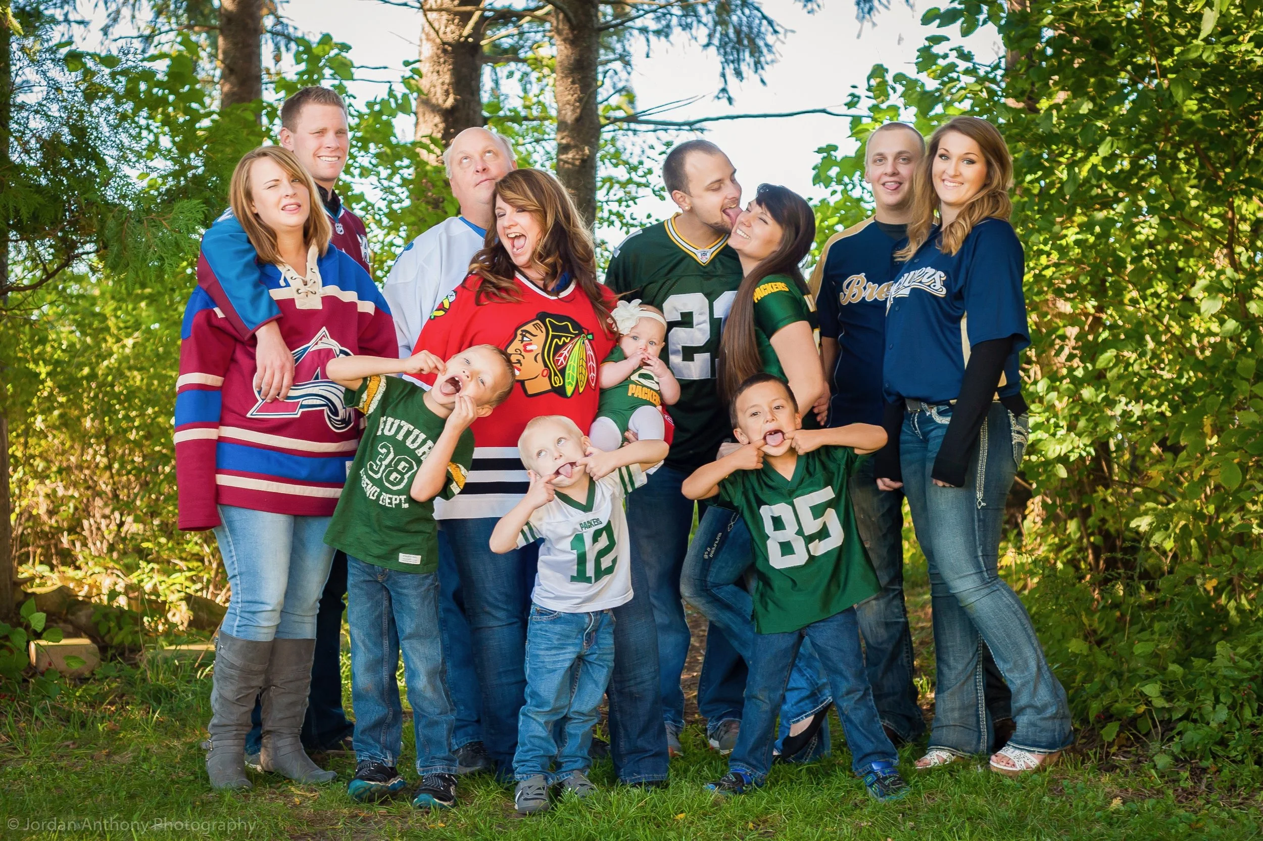 Family and children wearing sports jerseys posing outdoors in front of trees.