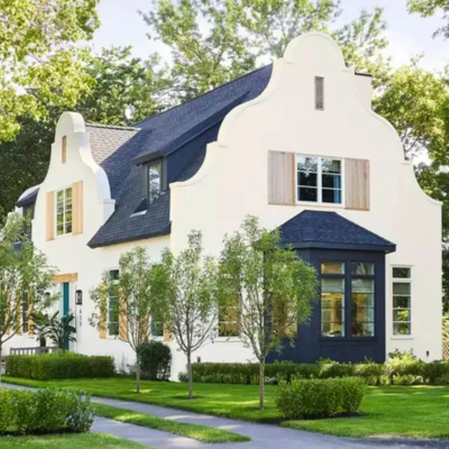 A modern home with a curved design painted in a cream with a bold navy roof and bay window, framed by a bright green grass and small trees.