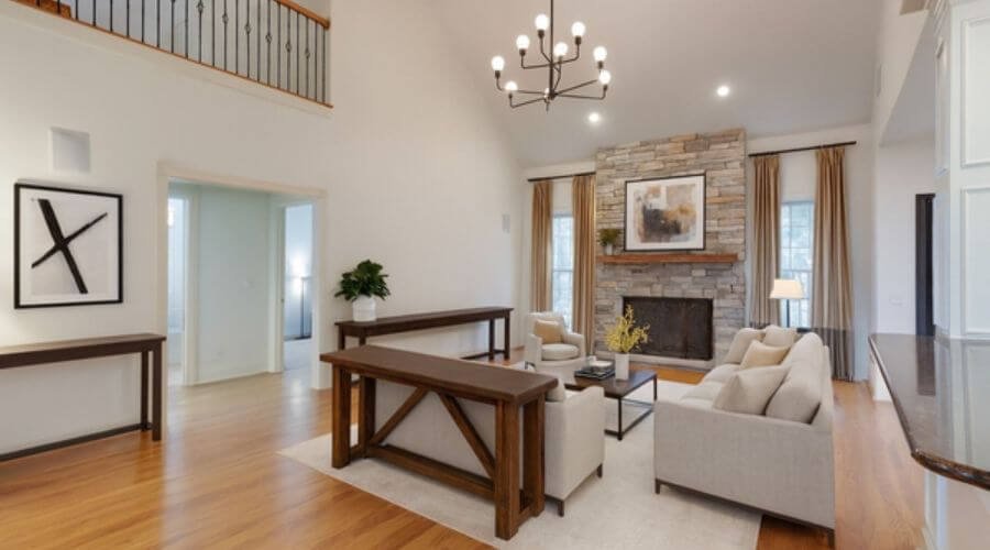 A home in southeast Nashville featuring a two-story living room with modern chandelier, light-stoned fireplace, and bright furniture with sand-wood accents.