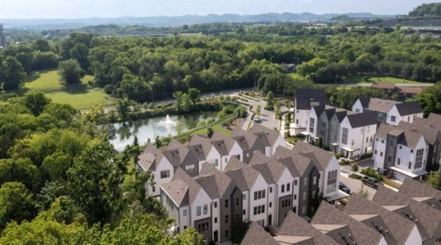 Aerial view of an East Nashville community featuring white multi-story townhomes with rolling hills and green trees surrounding the buildings.