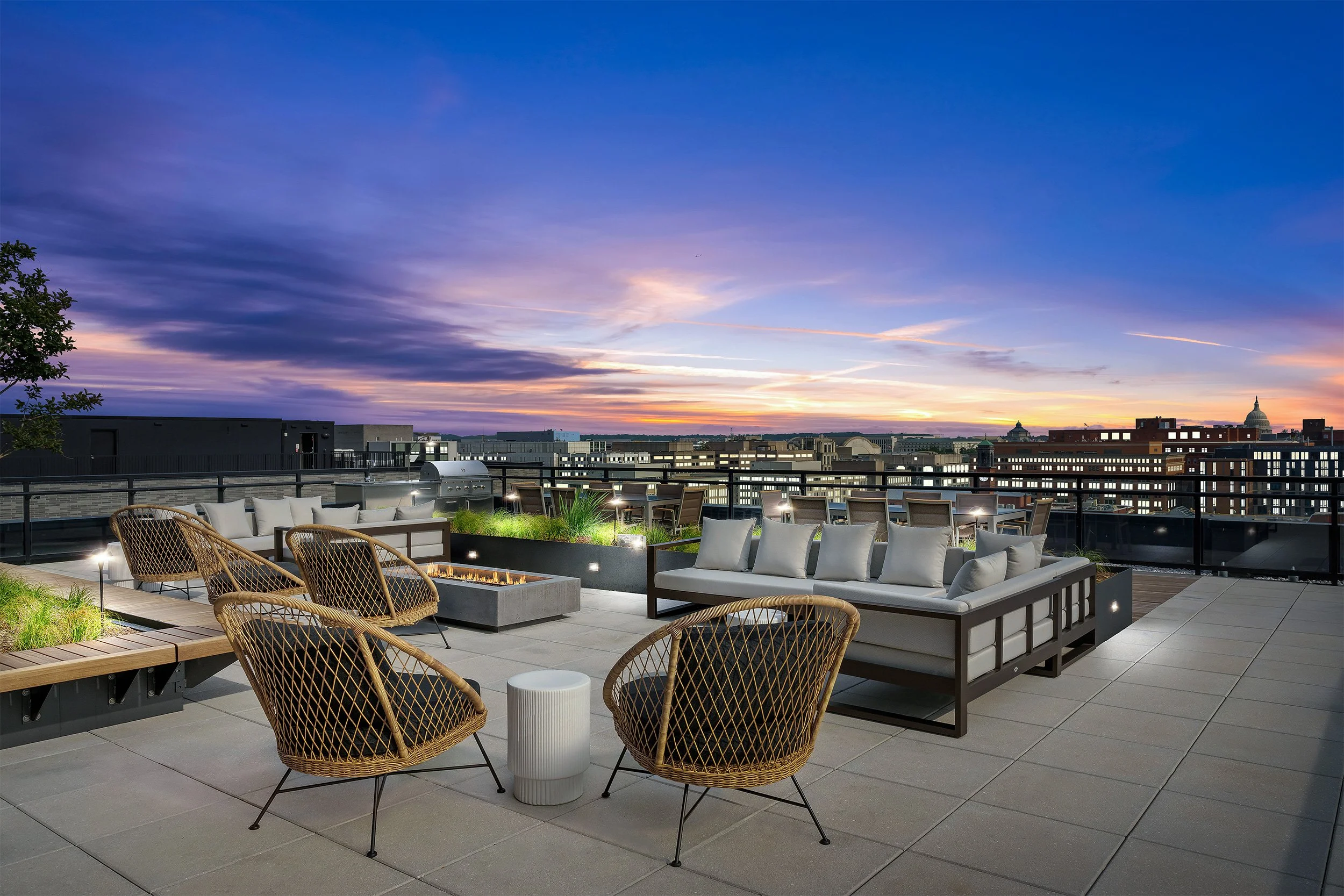 Rooftop terrace with outdoor seating, fire pit, and city skyline during sunset in Washington, DC.