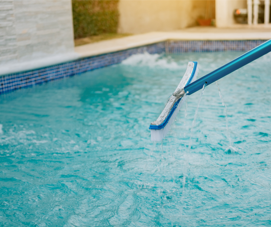 A swimming pool being cleaned with a brush on a long handle, water splashing.