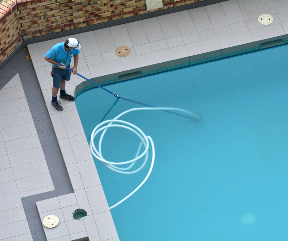 Person cleaning a swimming pool with a vacuum and hose