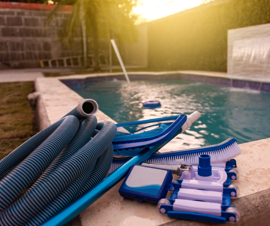 Pool cleaning equipment near a swimming pool with a hose, brush, and net. Background features pool edge and sunset lighting.