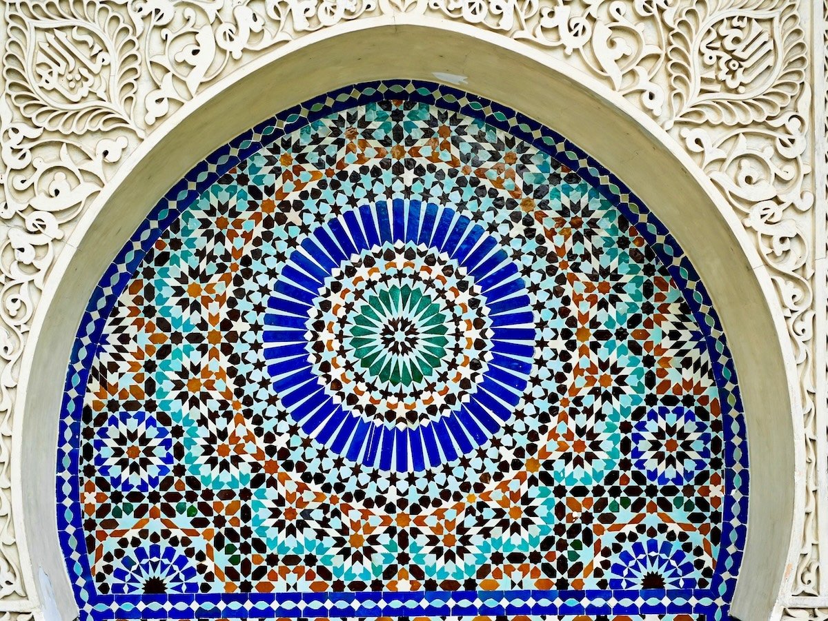 Colorful mosaic pattern embedded in an ornate arch with carved white decorative border.