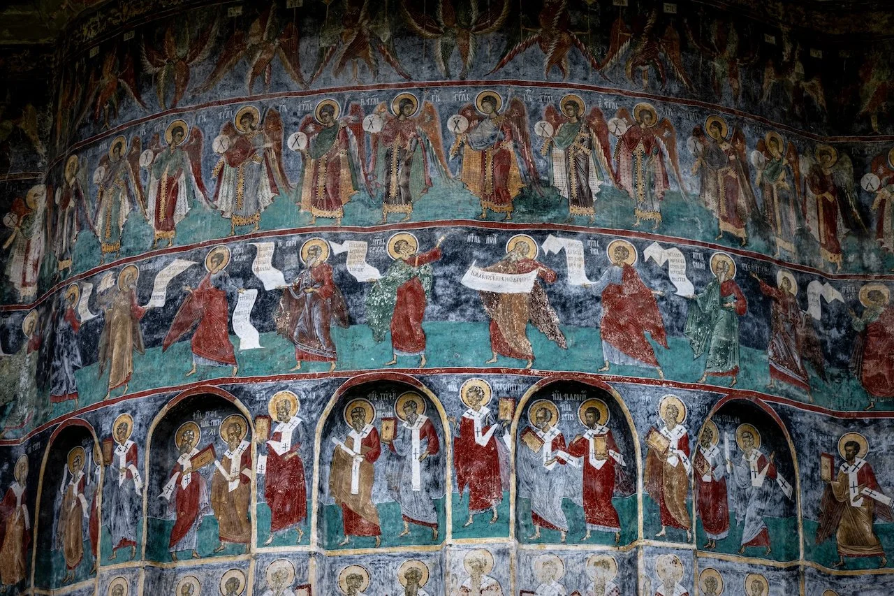 Interior of an ancient Christian church with religious frescoes depicting saints and biblical scenes on the walls.