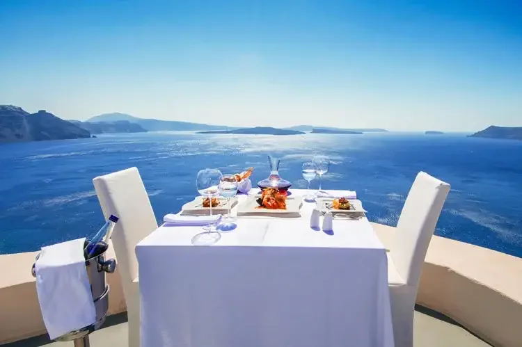 Greek tomatoes and olives with a bottle of red wine sit on a table overlooking Santorini's crater