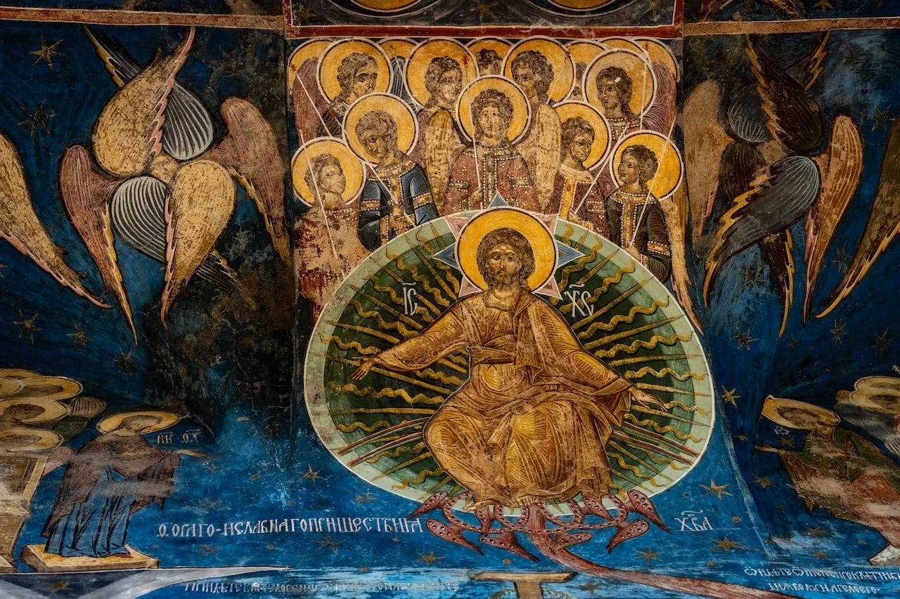 A religious fresco depicting Jesus Christ in the center with a halo, surrounded by angels and saints, with a dark background and decorative elements.