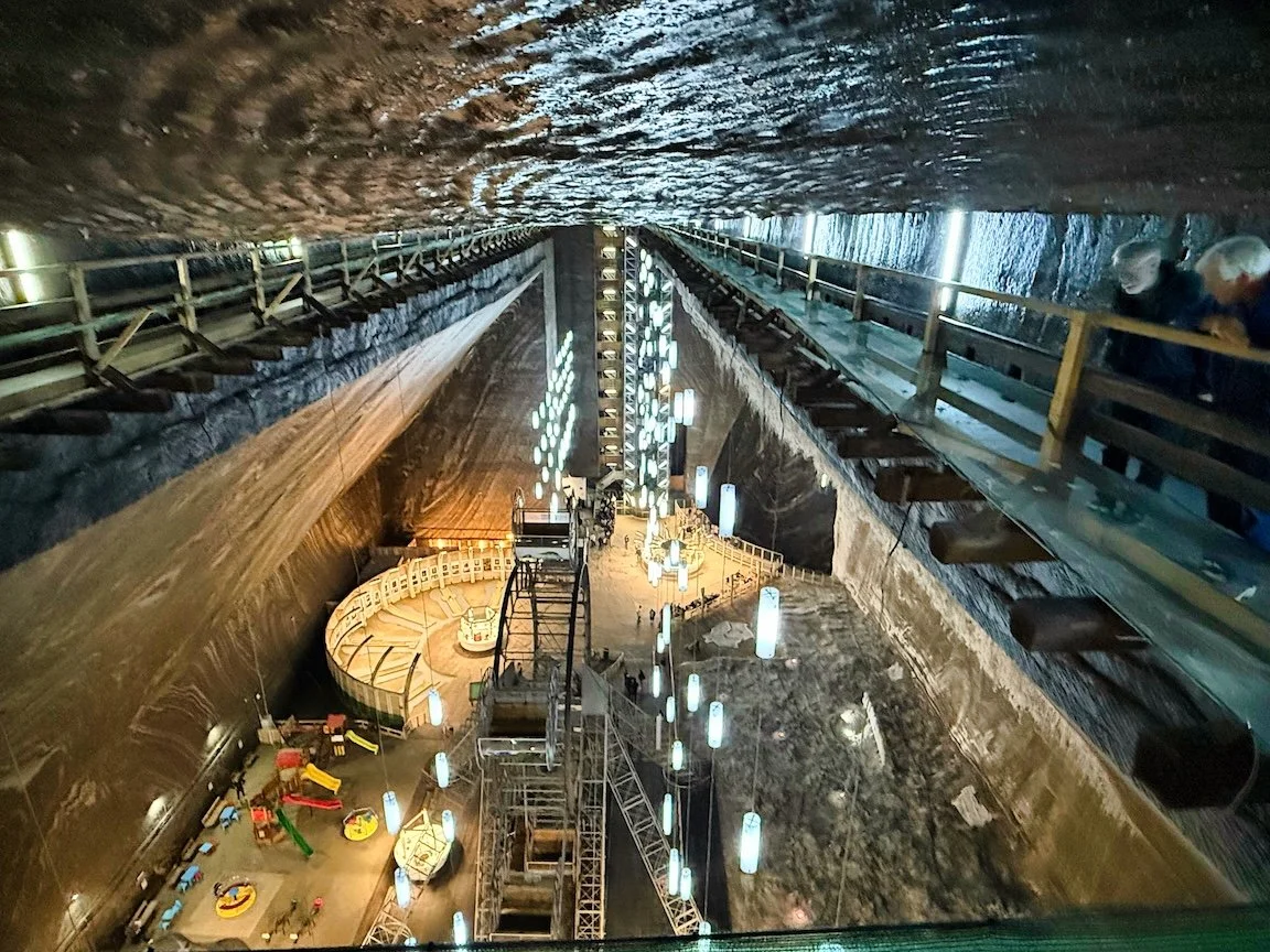 View of the inside of a large underground tunnel with walkways, scaffolding, and lighting, looking down from the top, revealing a construction or maintenance area.