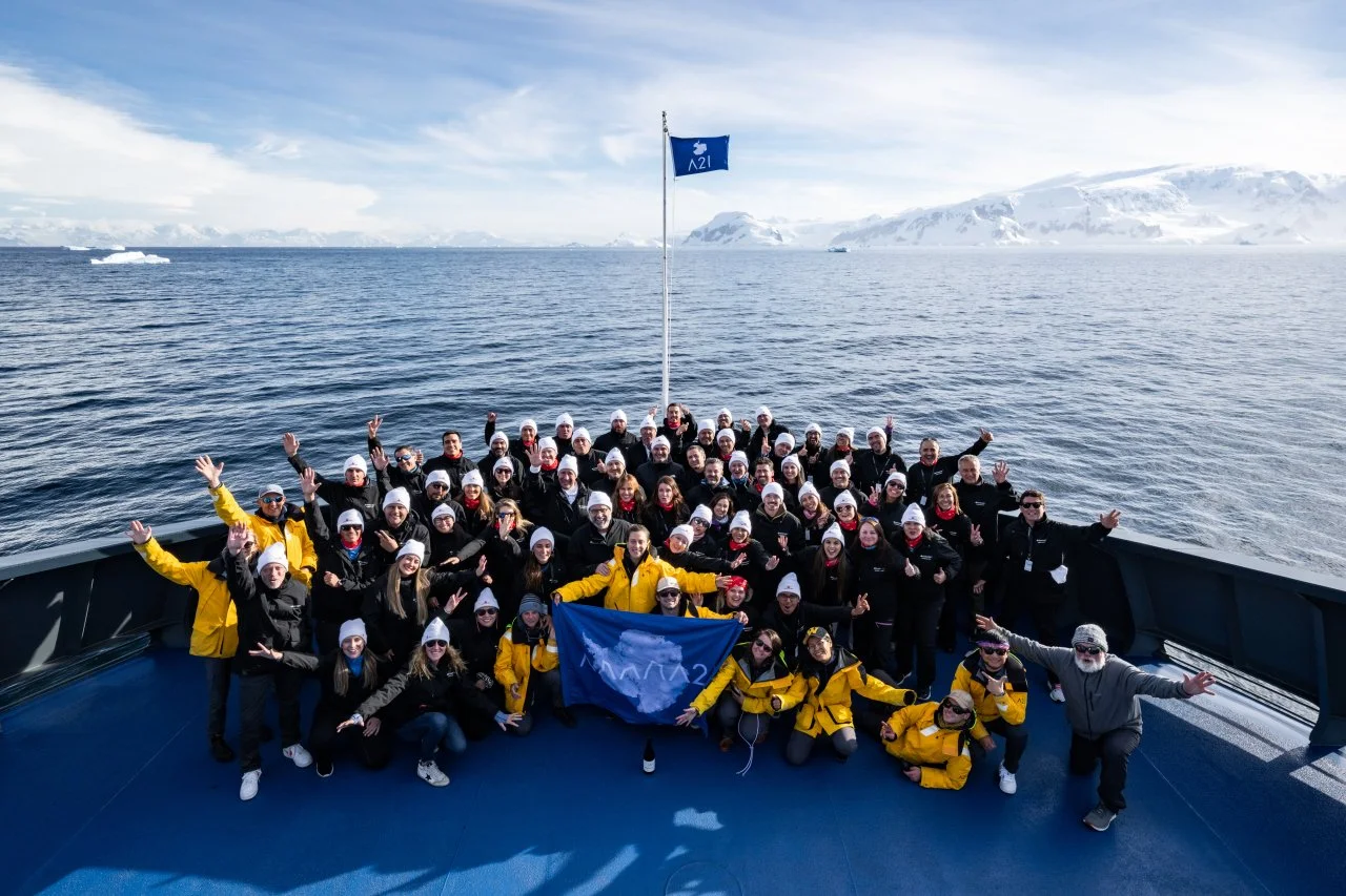 SMall-ship Antarctica expedition travelers gather for a group photo aboard the Magellan Discoverer front deck with arctic waters and snow-capped mountains behind