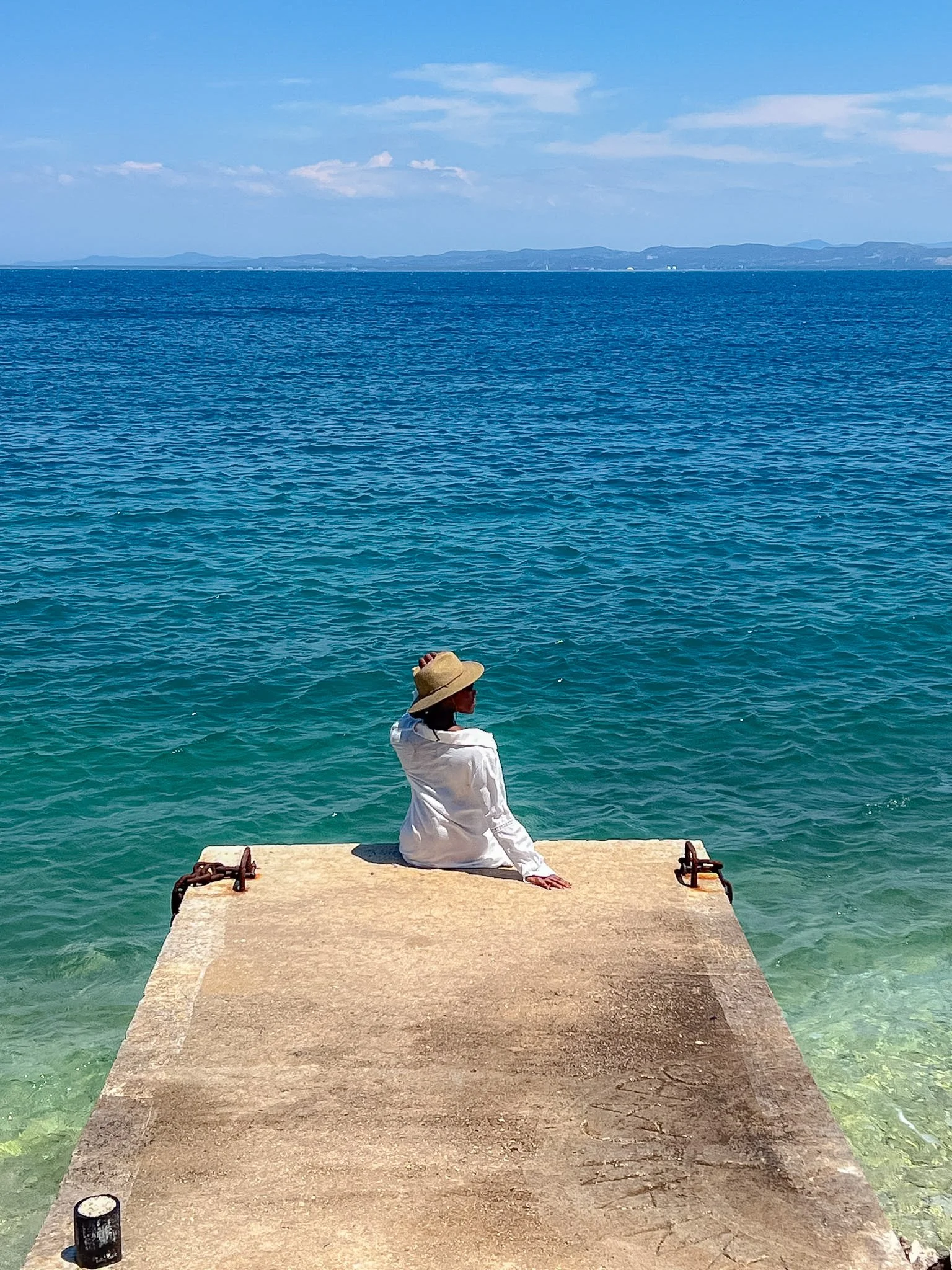 Woman in a sun hat sitting at the end of a stone pier over the Adriatic Sea, Vlore, Albania