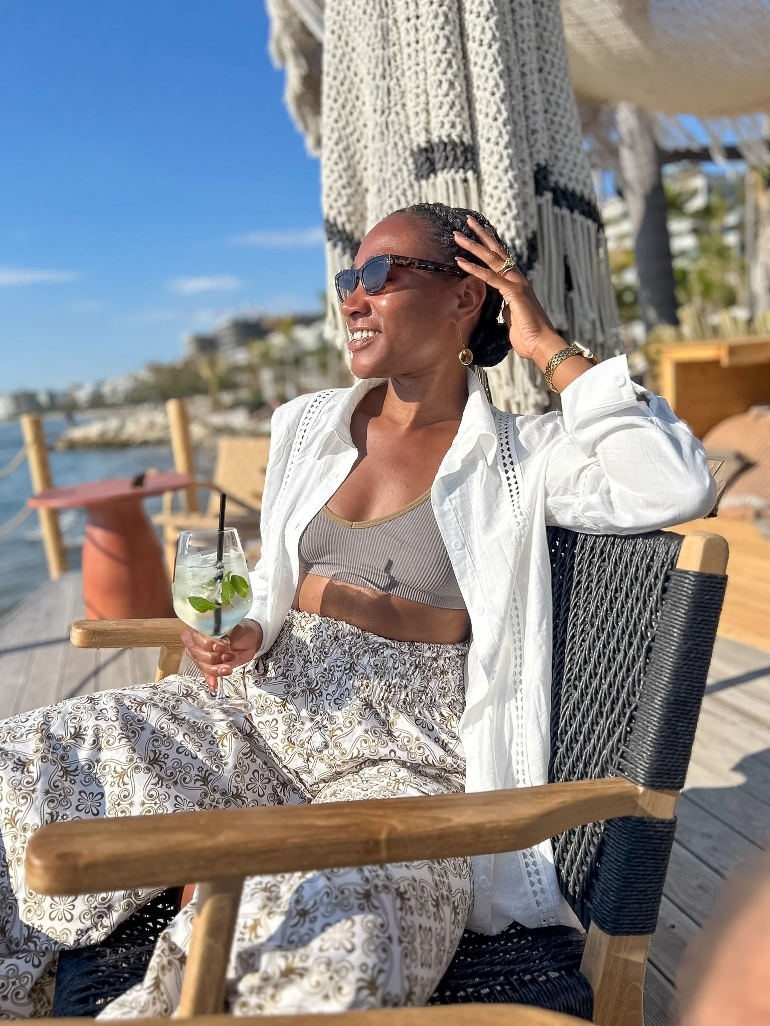 Woman in sunglasses and a white blazer relaxing with a cocktail at a seaside lounge, Vlore, Albania