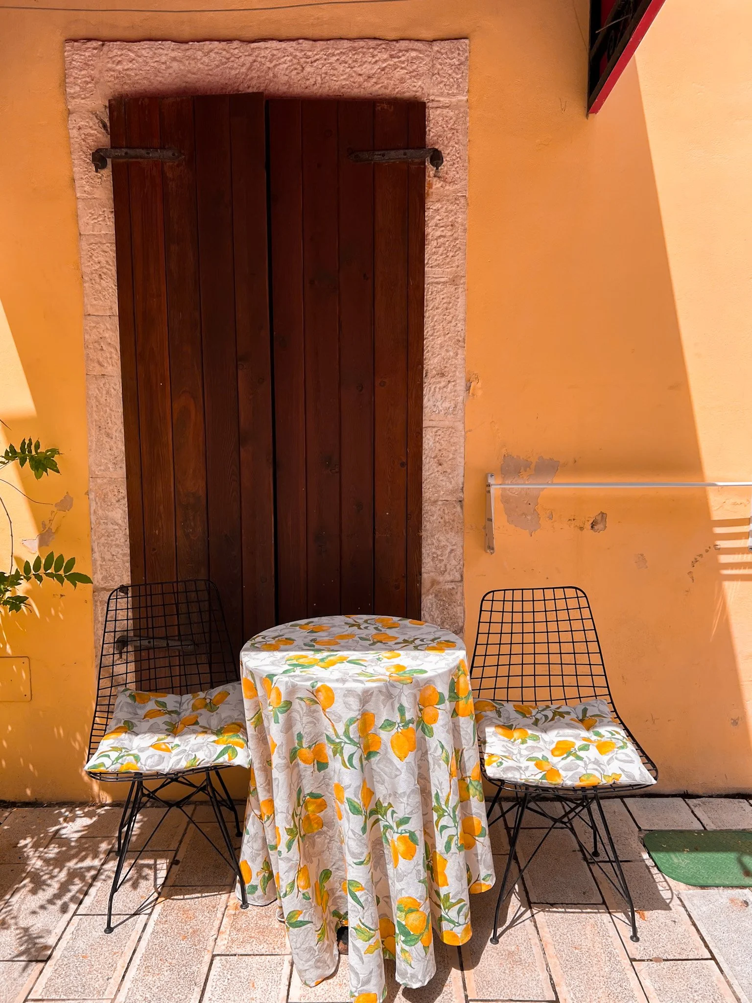 Lemon-print tablecloth on a small table with two chairs against an orange wall, Vlore Old Town, Albania