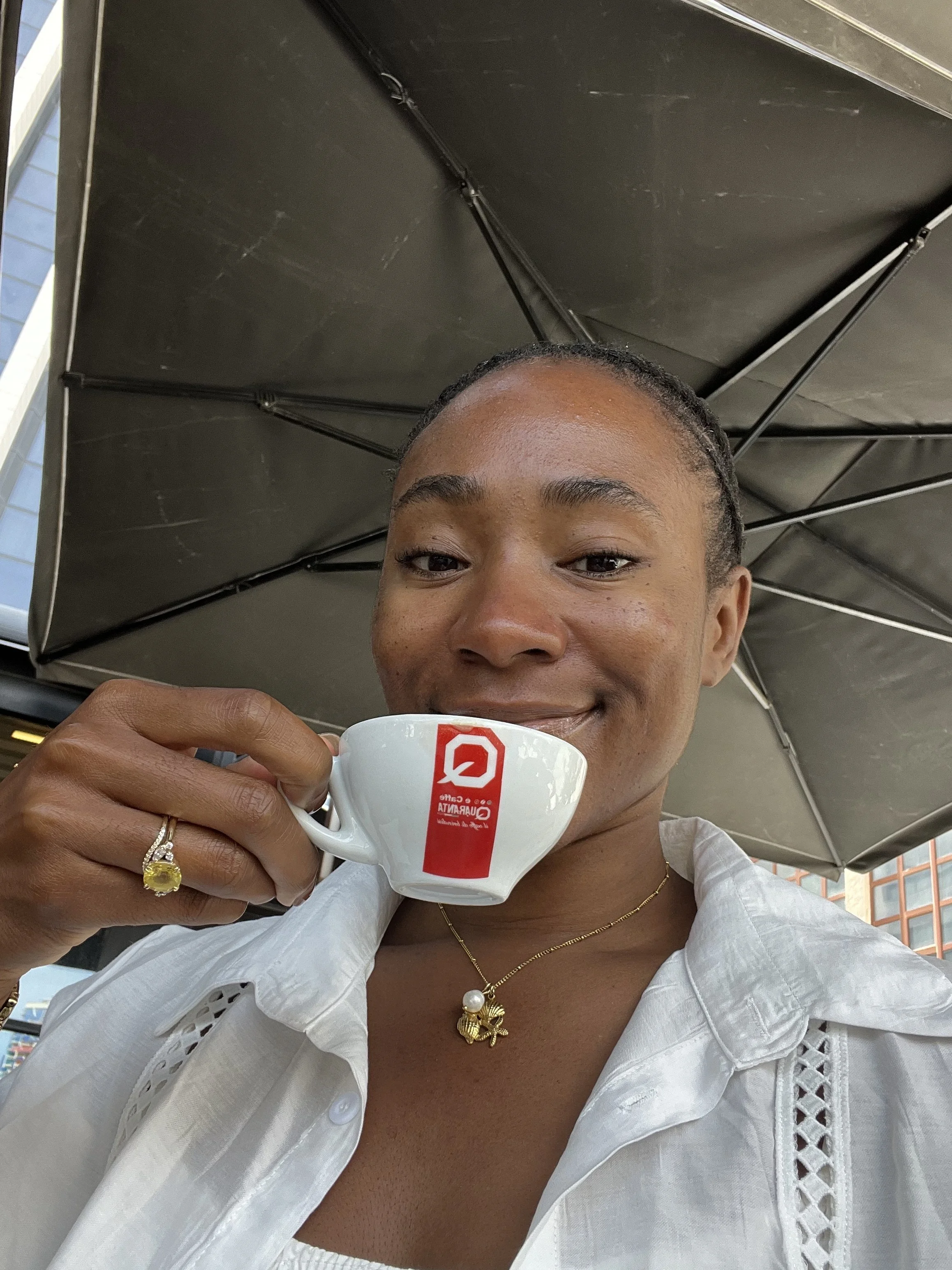 Smiling woman sipping espresso under a café umbrella, Vlore, Albania