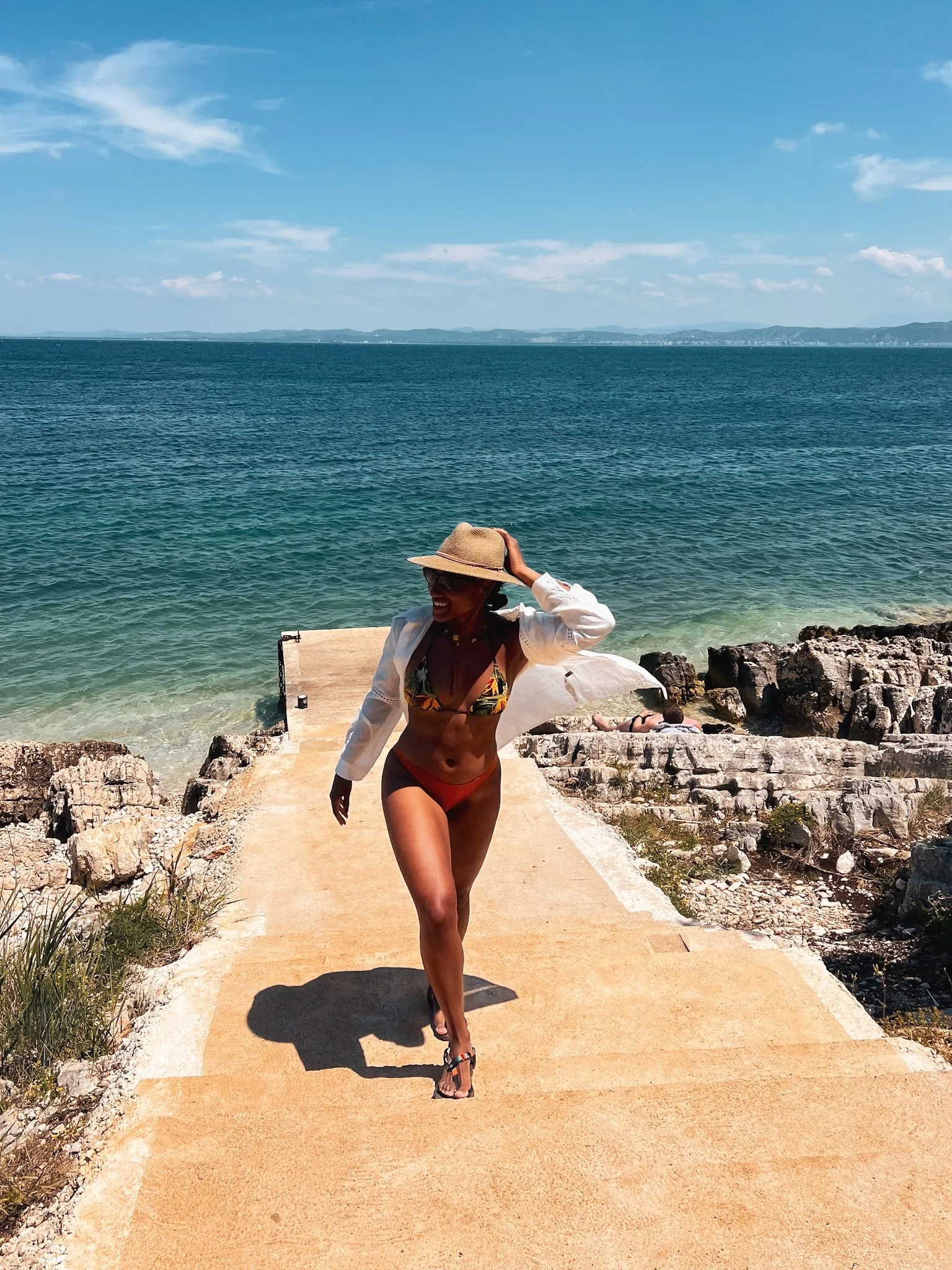 Woman in a sun hat walking up a stone path from the sea, Vlore, Albania