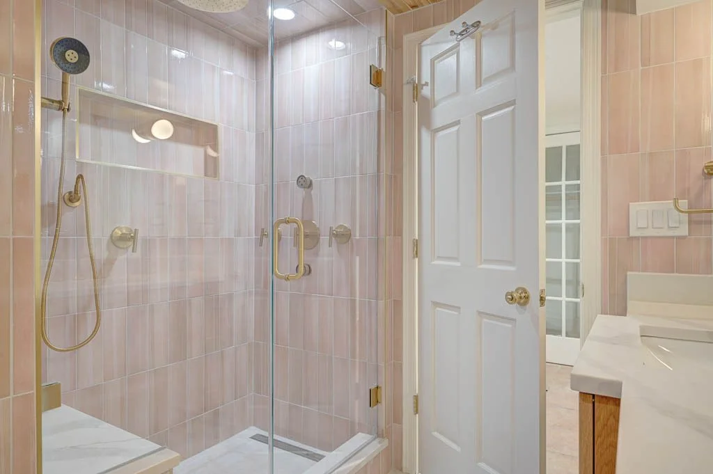 Bathroom with a glass shower door, pink tiled walls, a white door, and a marble countertop.