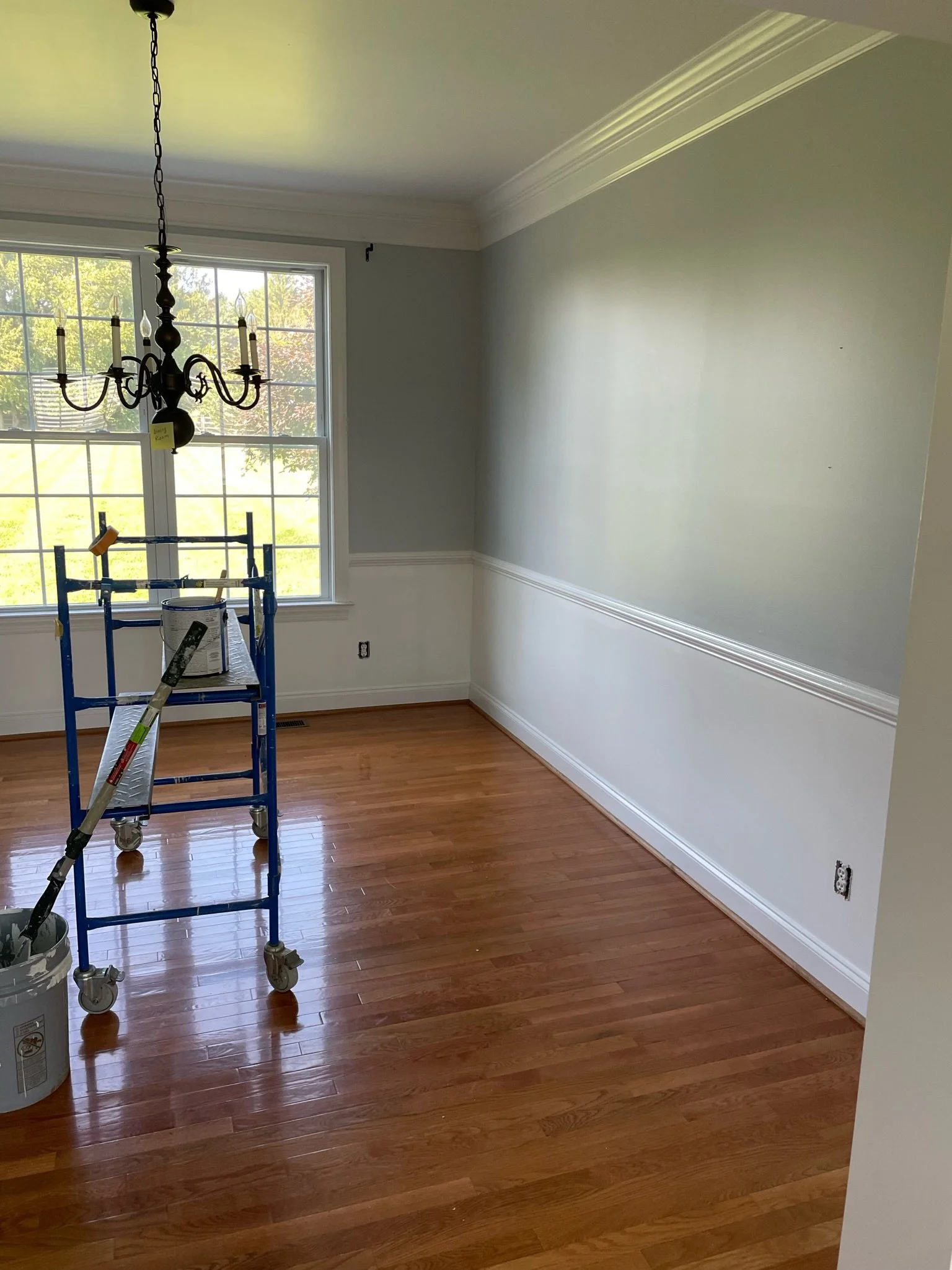 Empty dining room with hardwood floor, large window, chandelier, and wall with chair rail molding.