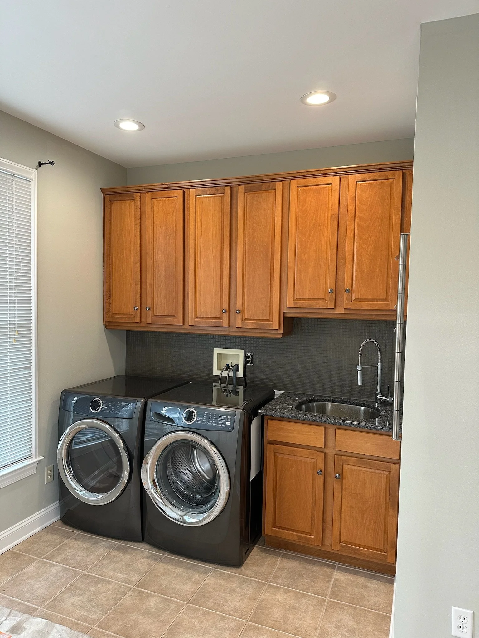 Laundry room with a front-loading washing machine and dryer, wooden cabinets, a small sink, and tiled floor.