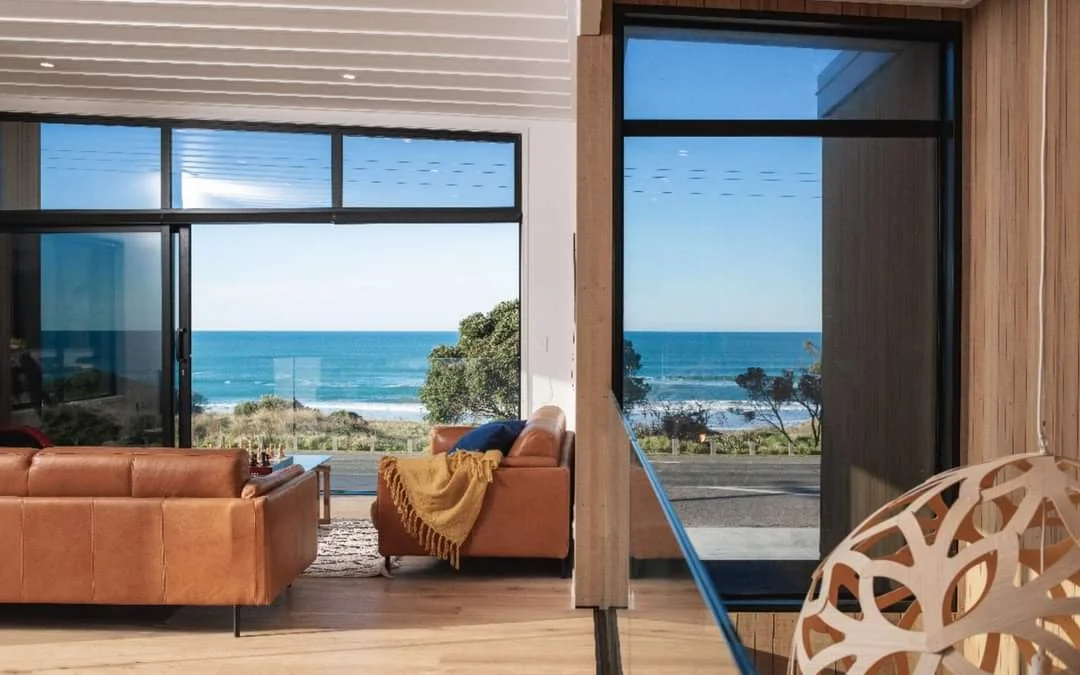 Living room with brown leather sofas, a yellow throw blanket, and large windows showing a beach and ocean view.