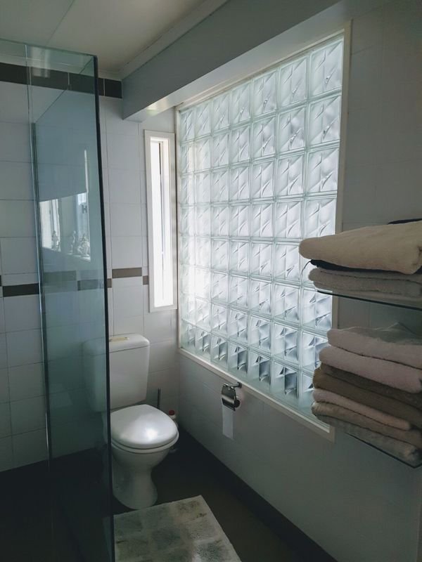 Small bathroom with glass block window, white toilet, towel shelf with folded towels, and partial glass shower enclosure.