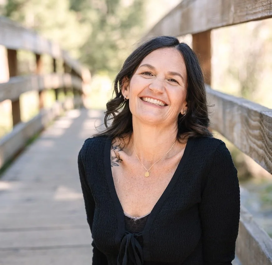 Woman with black hair smiling standing with a bridge behind her
