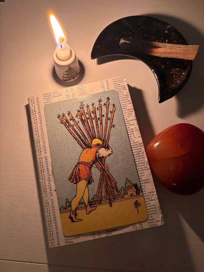 A man hunched over carrying 10 wands- a heavy burden towards a small village in the background