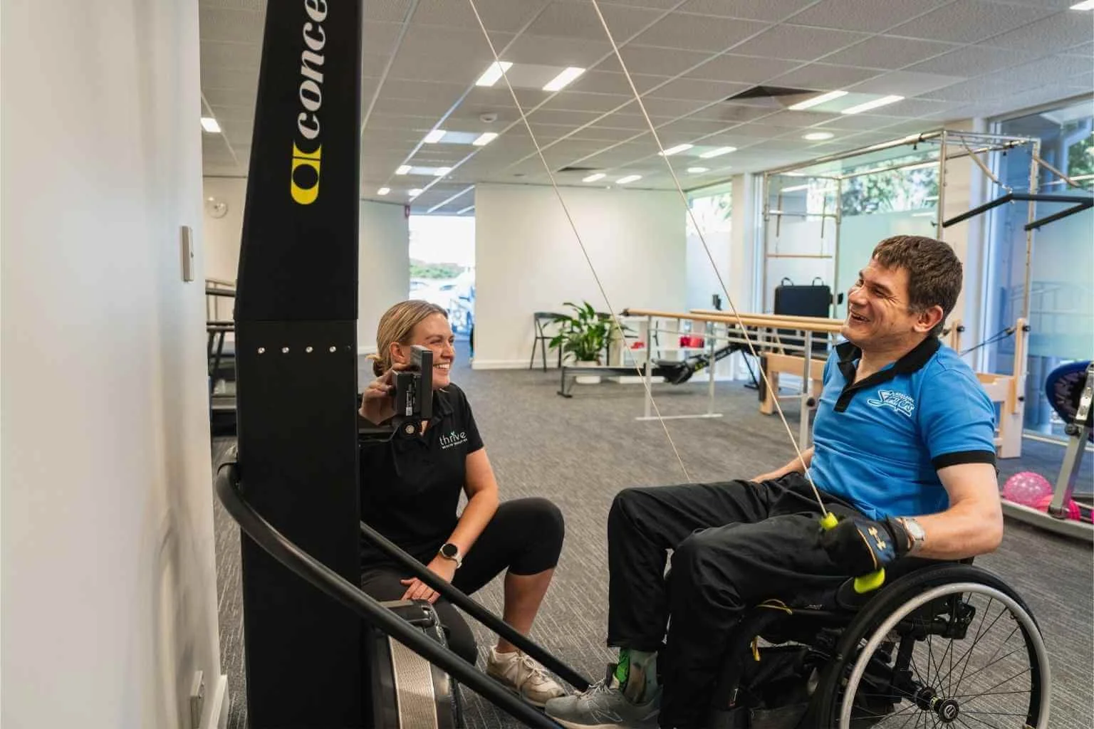Occupational therapist and client laughing together during a wheelchair assessment using exercise equipment at our clinic in Findon