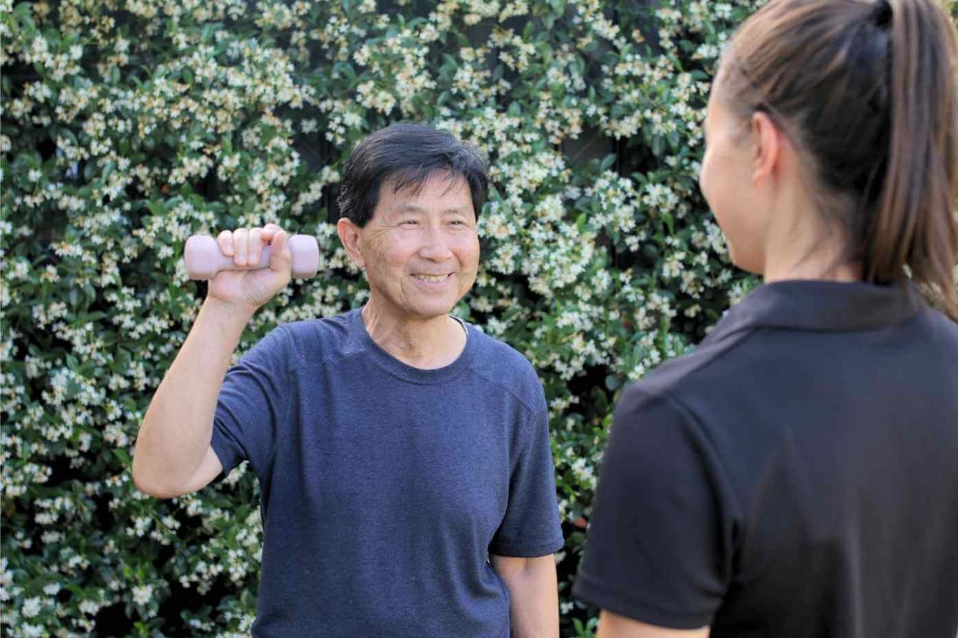 Client smiling whilst using dumbbell at home during a mobile neurological physiotherapy visit
