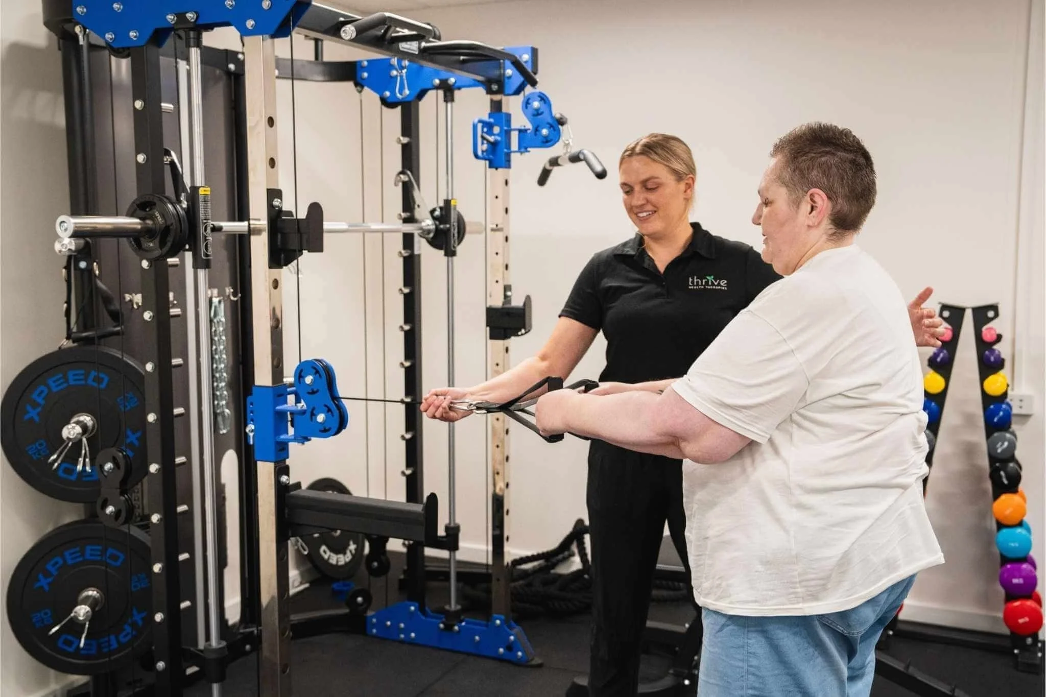 Physiotherapist smiling assisting client who is using a  strength training equipment at our Findon clinic